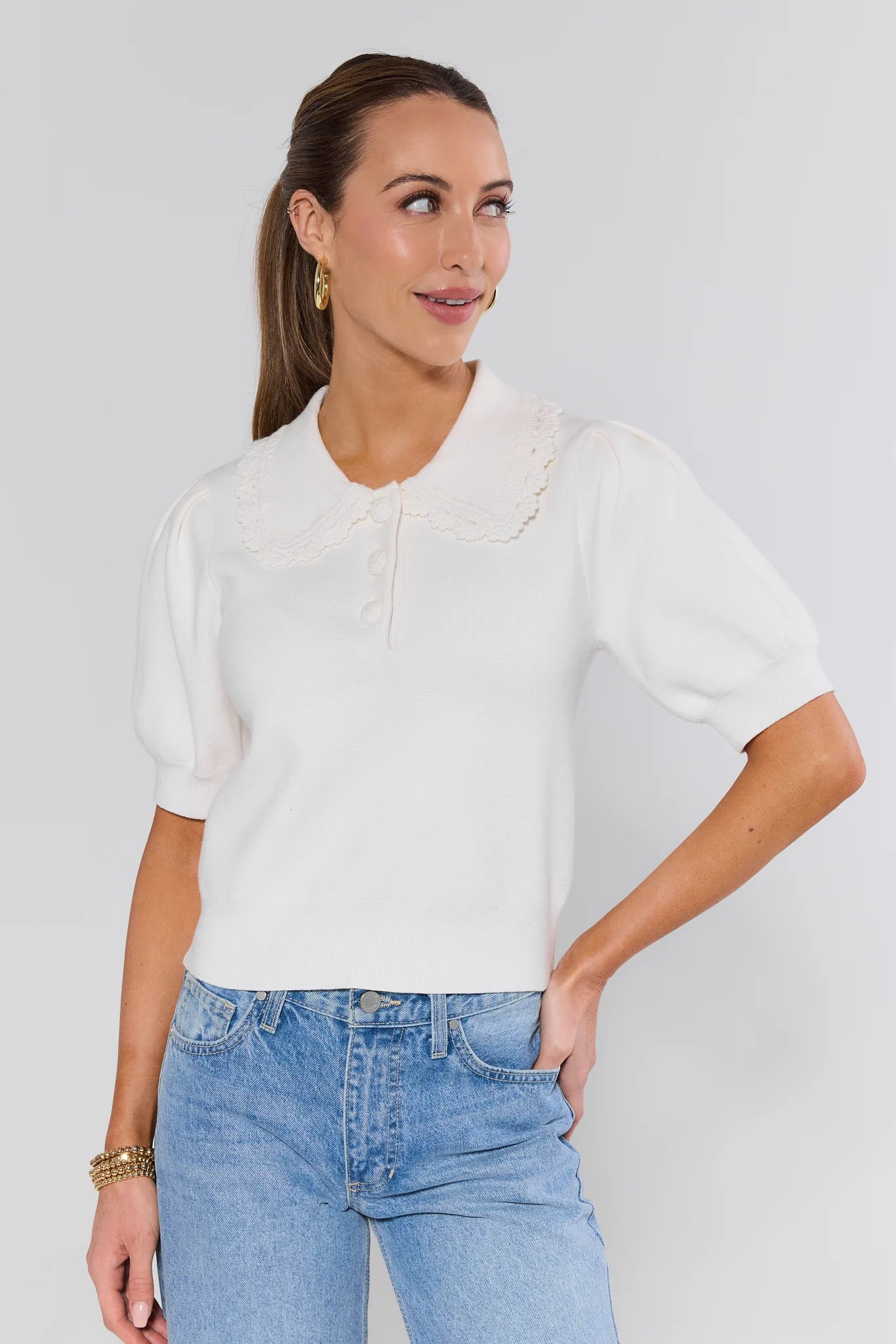 Woman wearing a white blouse and blue jeans against a plain background