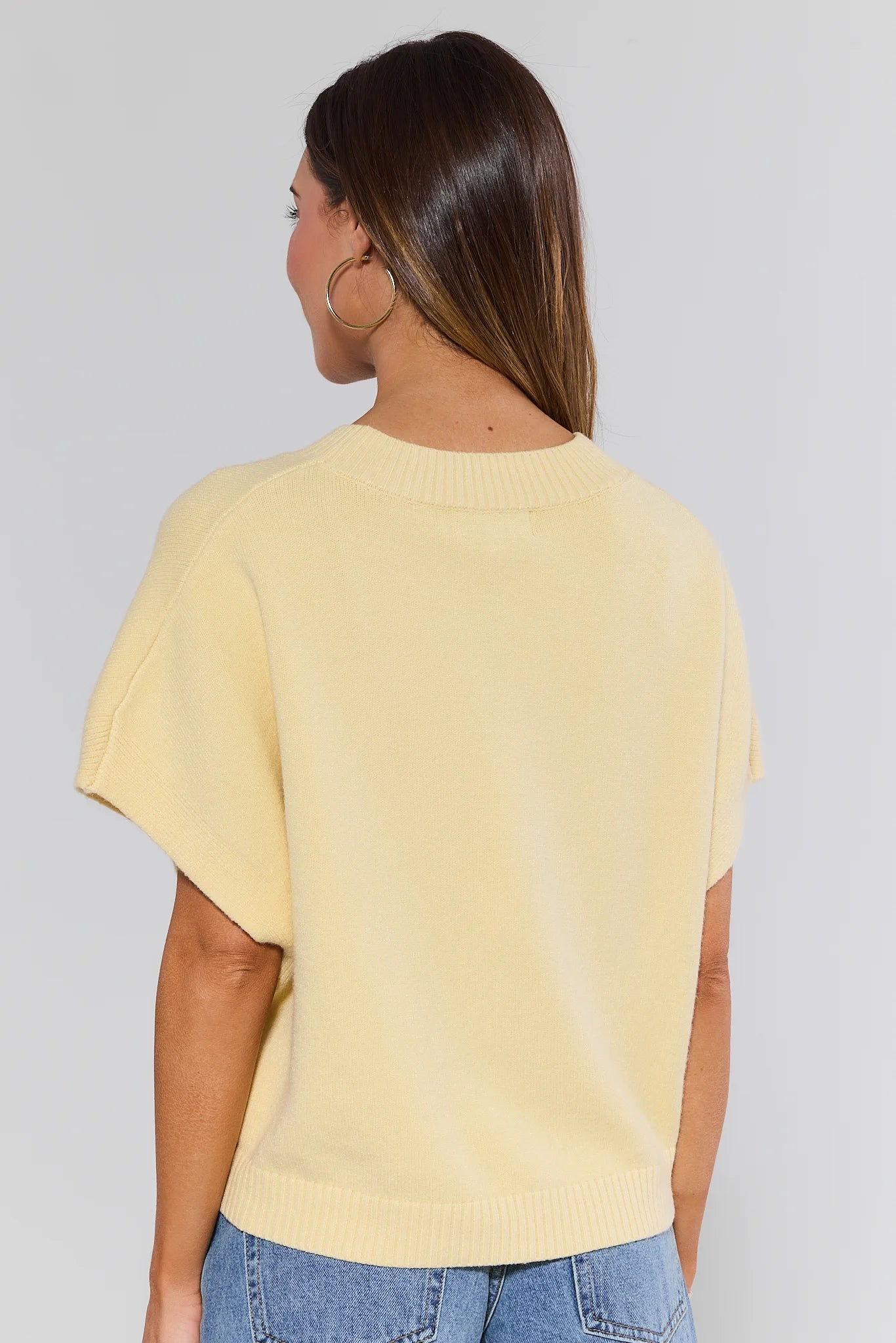 Woman wearing a yellow top and blue jeans against a plain background
