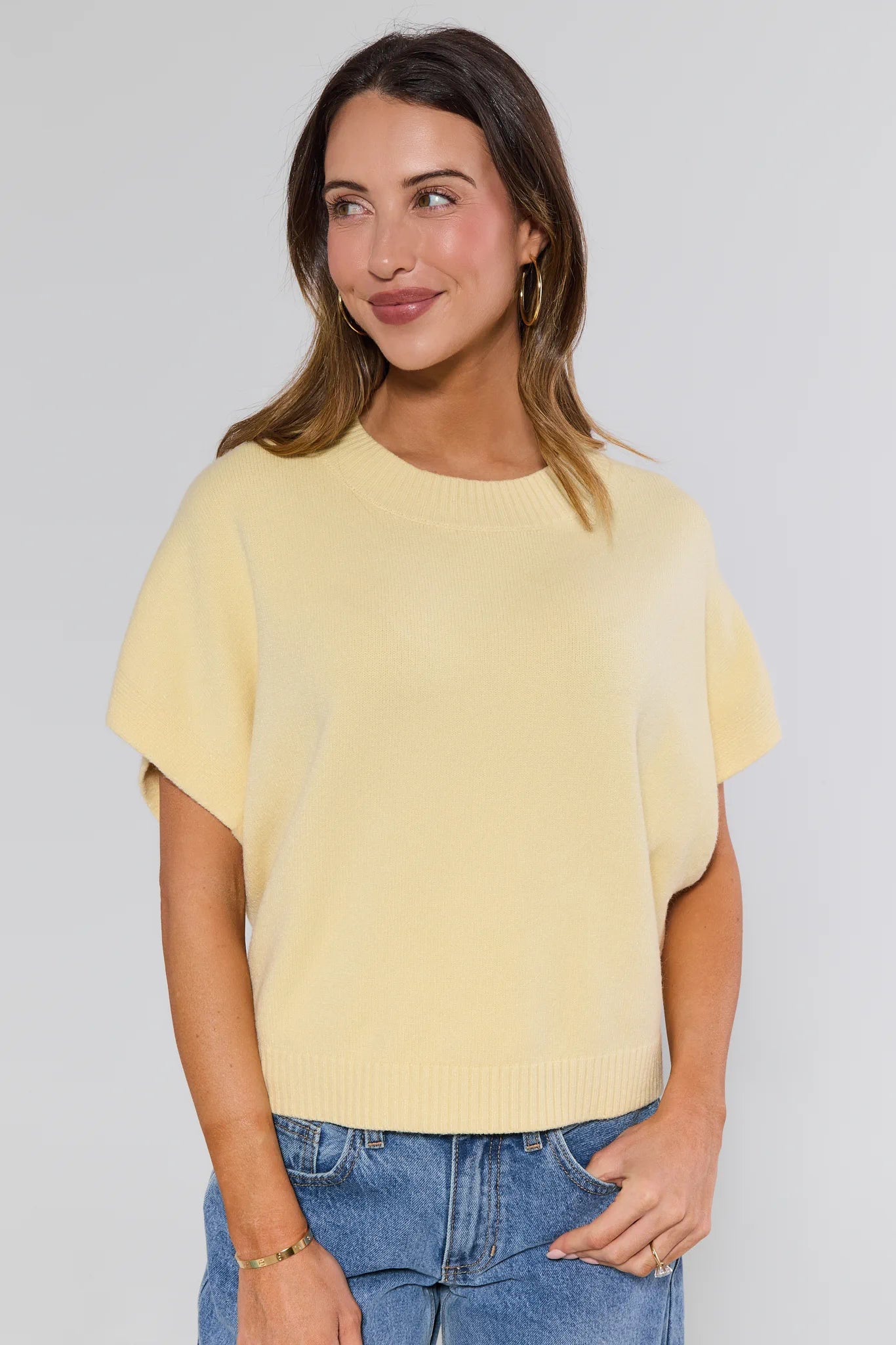 Woman wearing a yellow top and blue jeans against a plain background