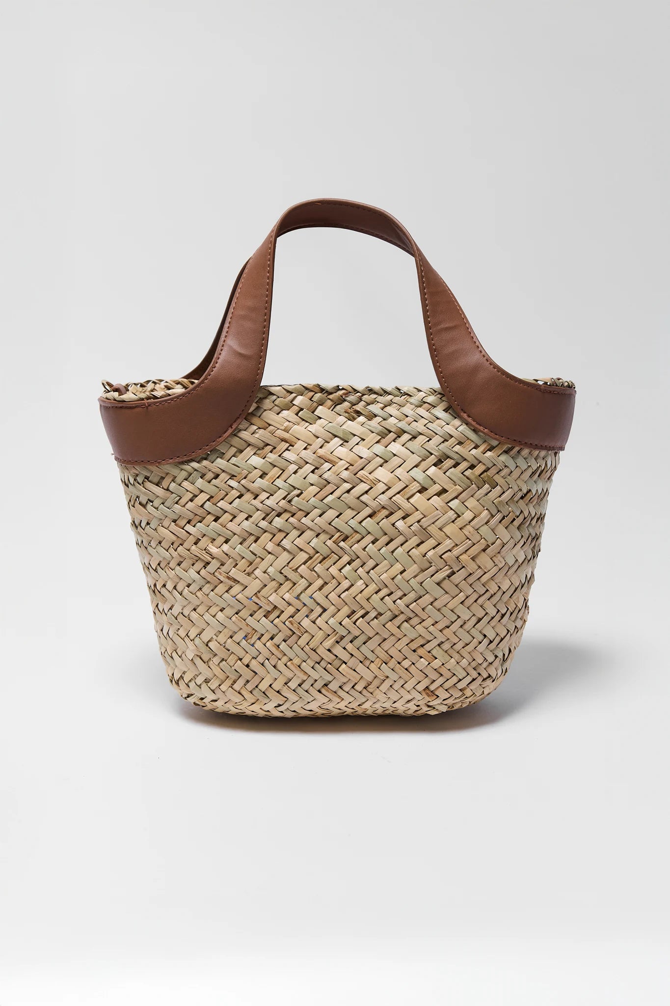 Woven straw bag with brown leather handles on a light gray background