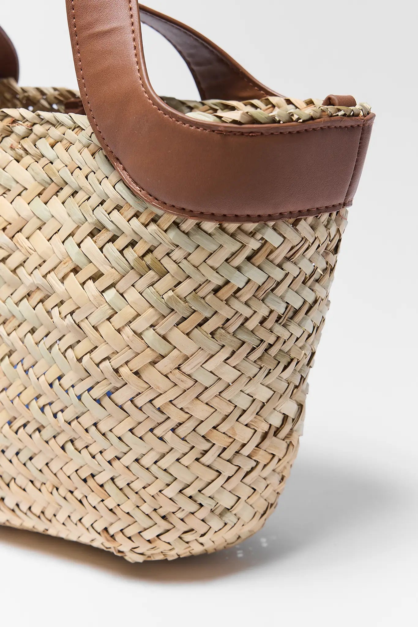 close up Woven handbag with brown leather handle on a light gray background