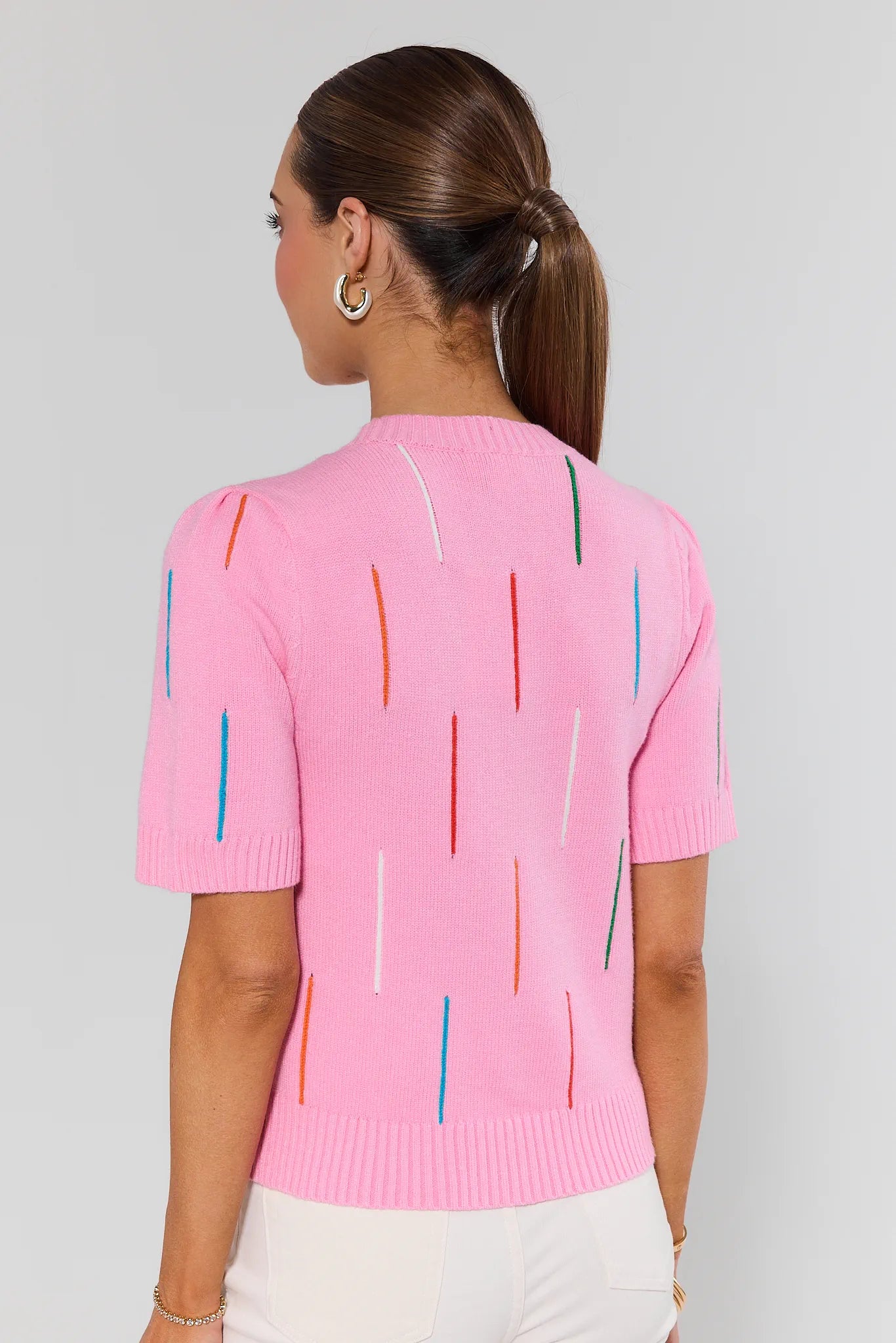 Woman wearing a pink sweater with colorful vertical stripes on a plain background