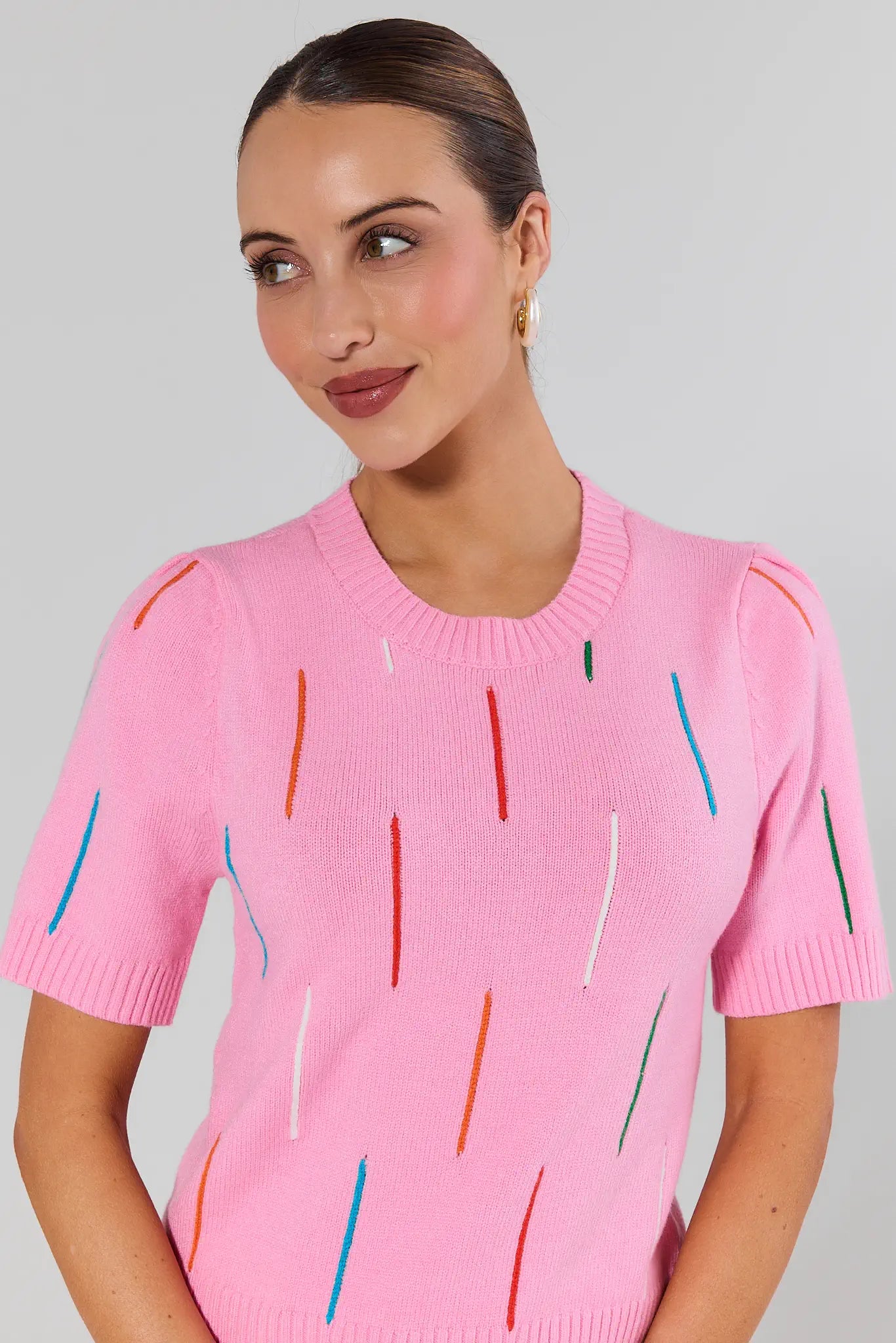 Woman wearing a pink sweater with colorful vertical stripes on a gray background