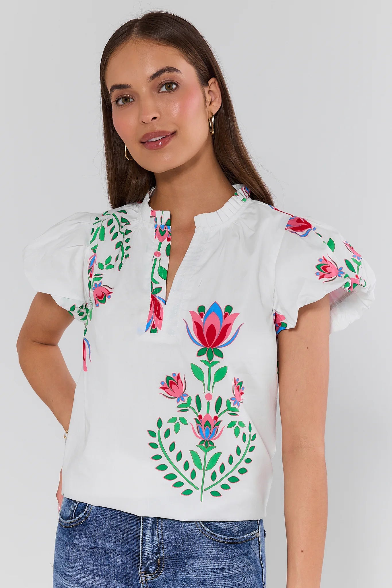 Woman wearing a white blouse with colorful floral embroidery on a plain background