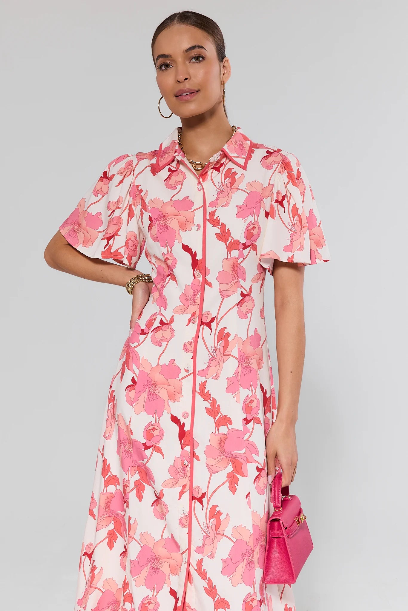 Woman wearing a pink floral dress holding a matching handbag against a gray background
