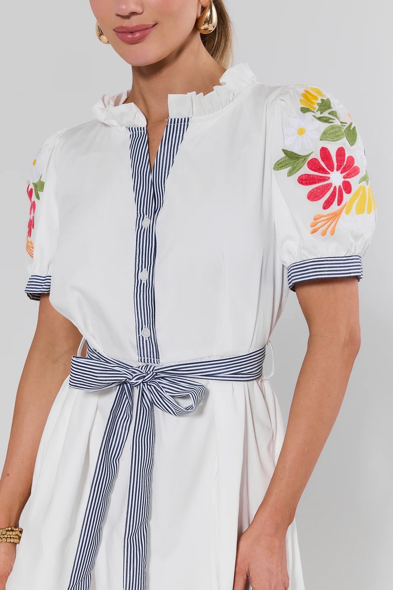 Woman wearing a white dress with colorful floral embroidery on a plain background