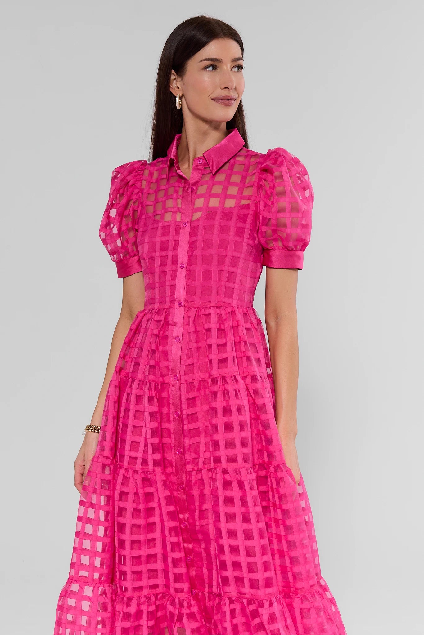 Woman wearing a bright pink dress with sheer overlay on a gray background