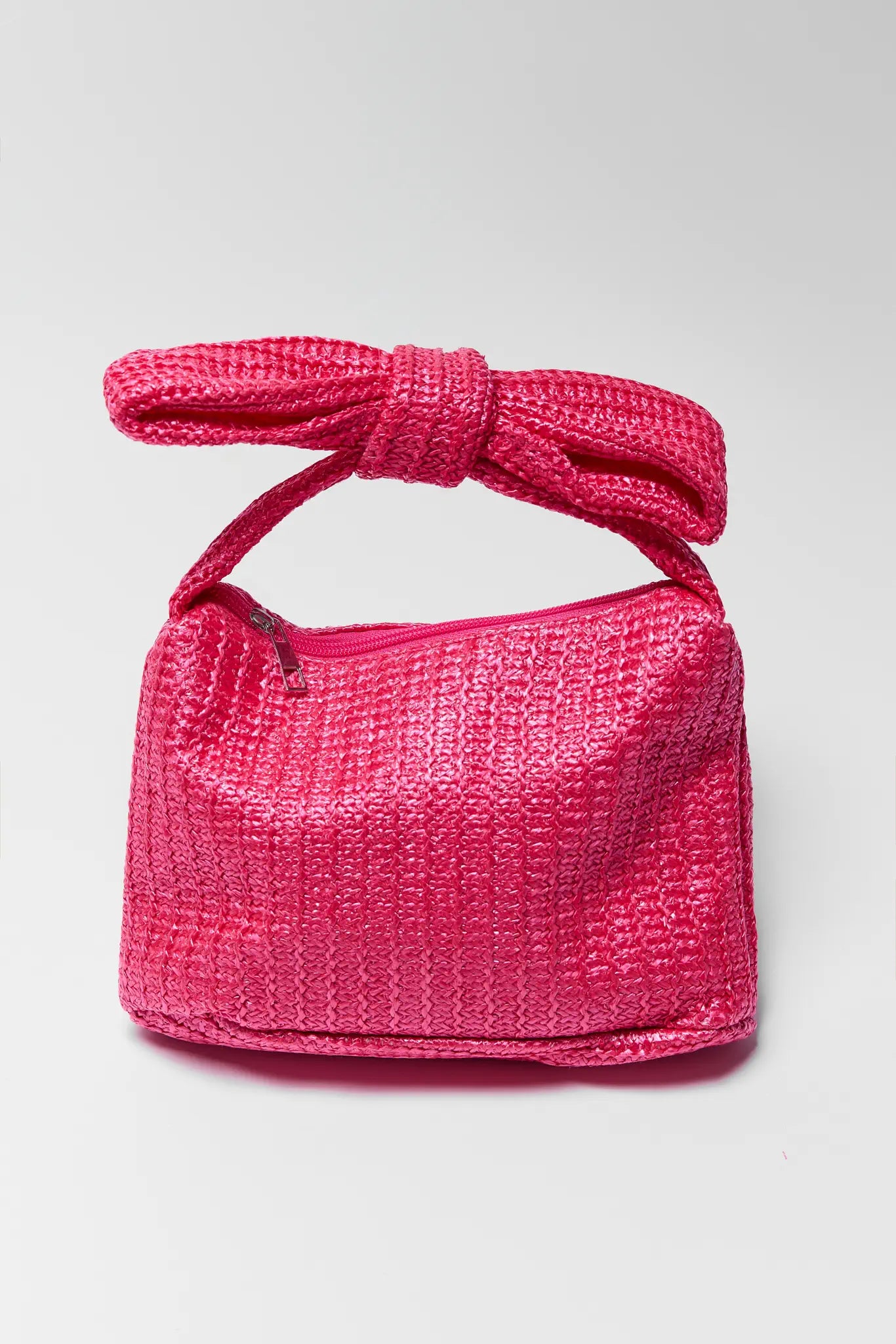 Pink woven handbag with a bow on a light gray background