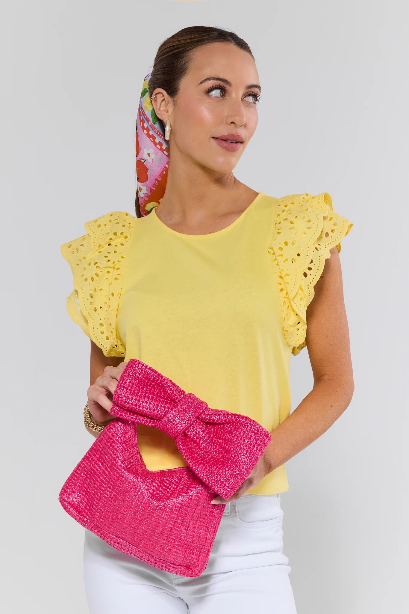 Woman wearing a yellow top with ruffled sleeves and holding a pink clutch against a white background
