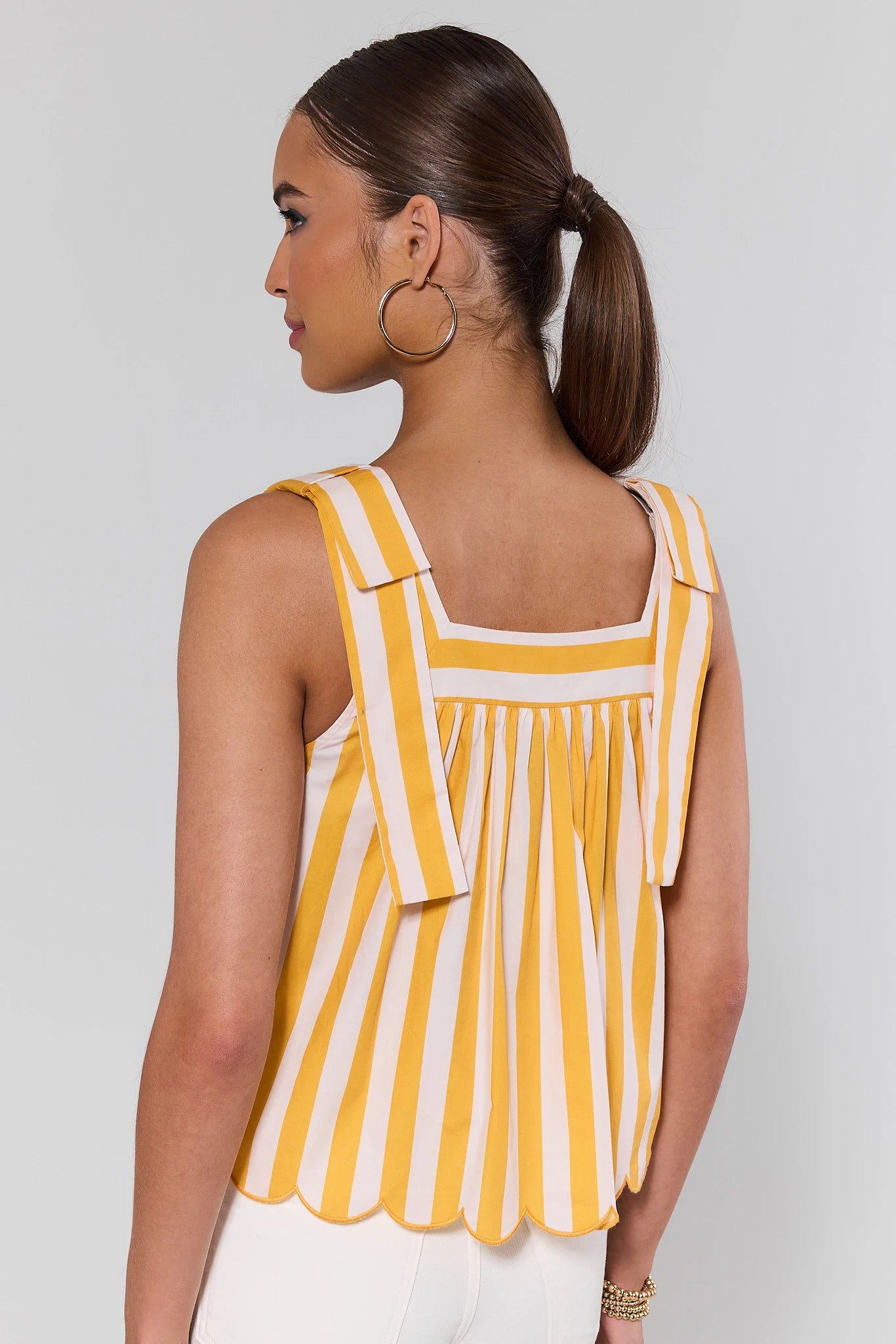 Woman standing wearing a yellow and white striped sleeveless top against a plain background