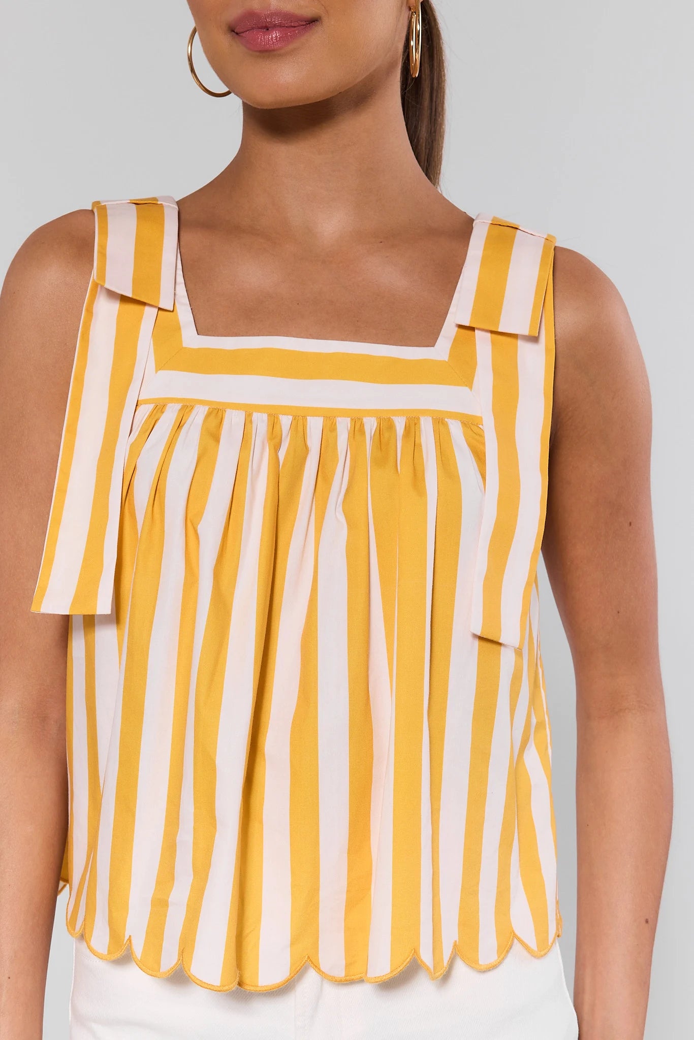 close up Yellow and white striped sleeveless top worn by a person on a plain background