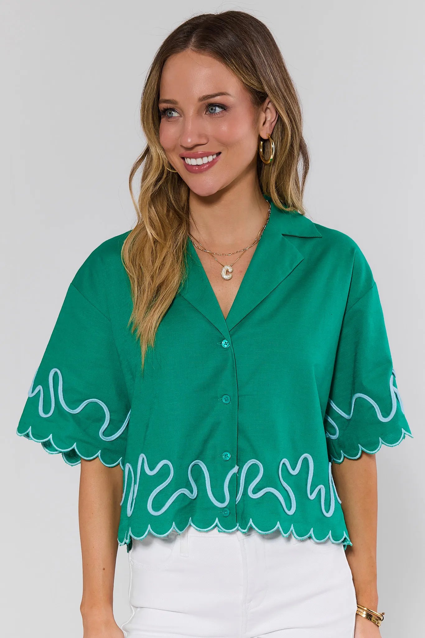 Woman wearing a green blouse with white scalloped edges on a plain background