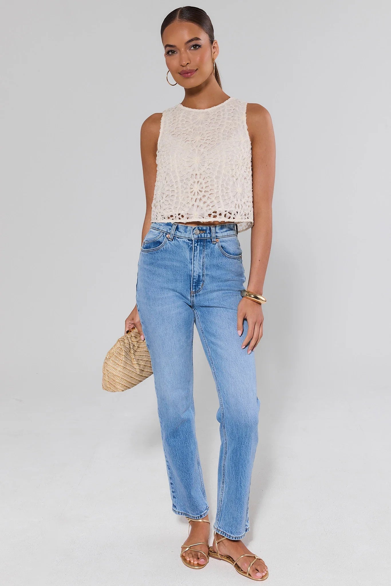 Woman wearing a sleeveless crochet top and blue jeans against a white background