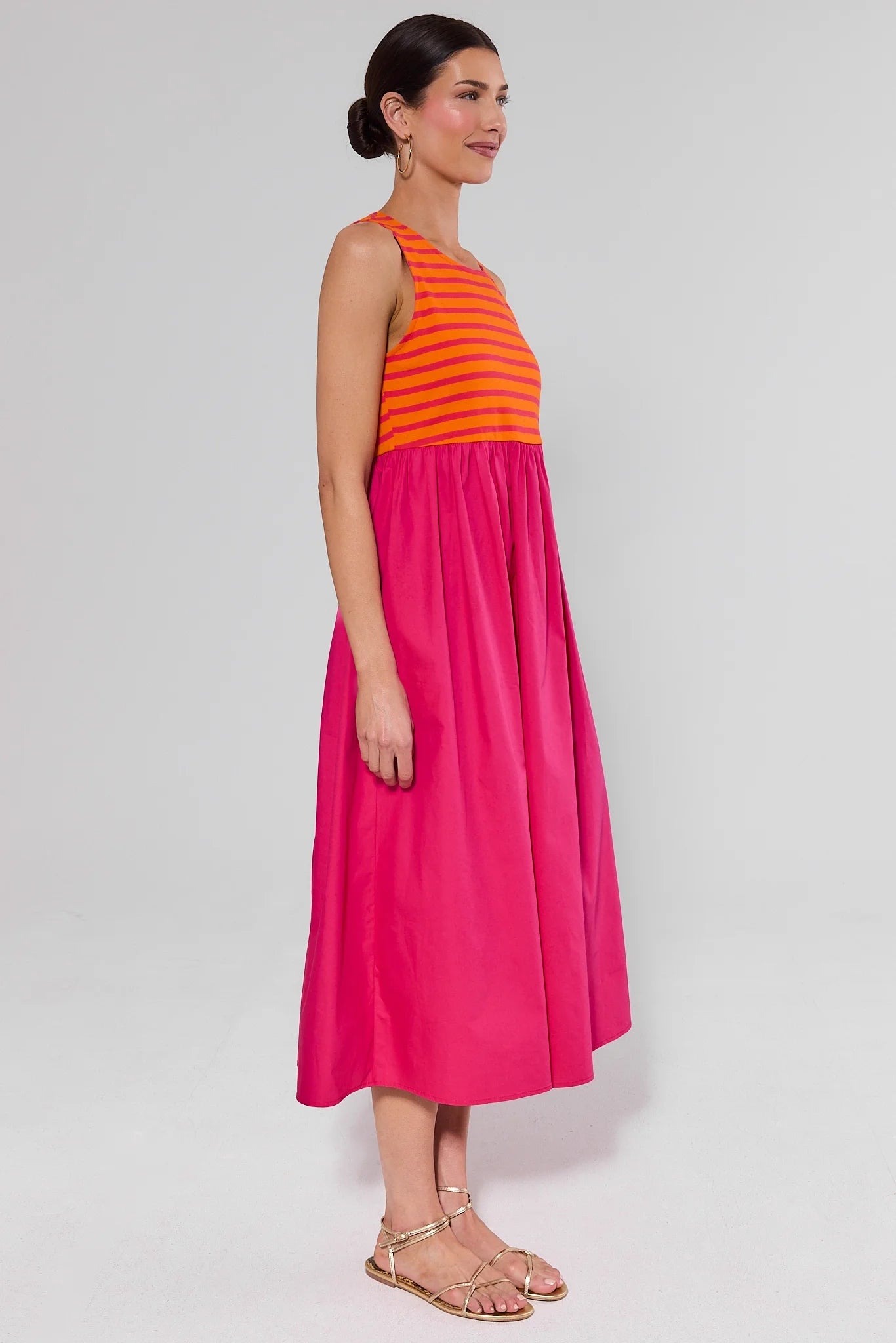 side shot Woman wearing a pink dress with an orange striped top on a white background