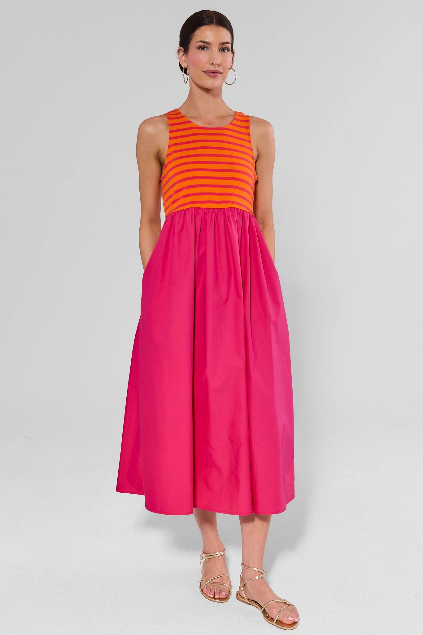 Woman wearing a bright pink dress over an orange striped top on a white background