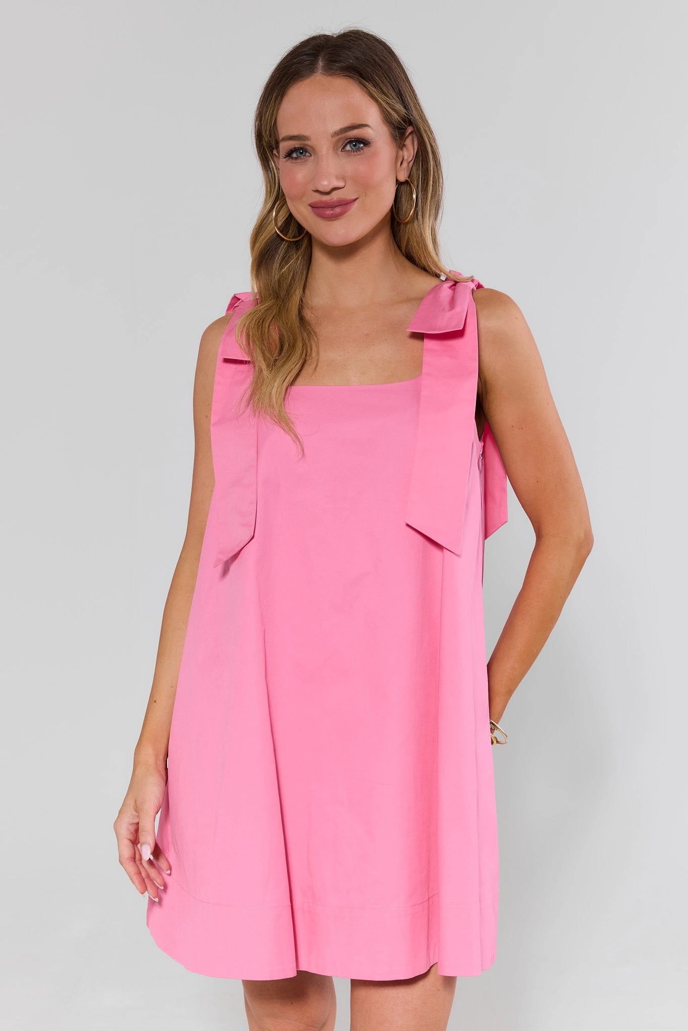 Woman wearing a pink dress with bow straps on a gray background