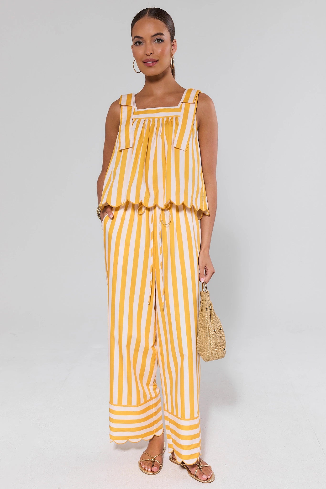 Woman wearing a yellow and white striped top and pants on a plain background