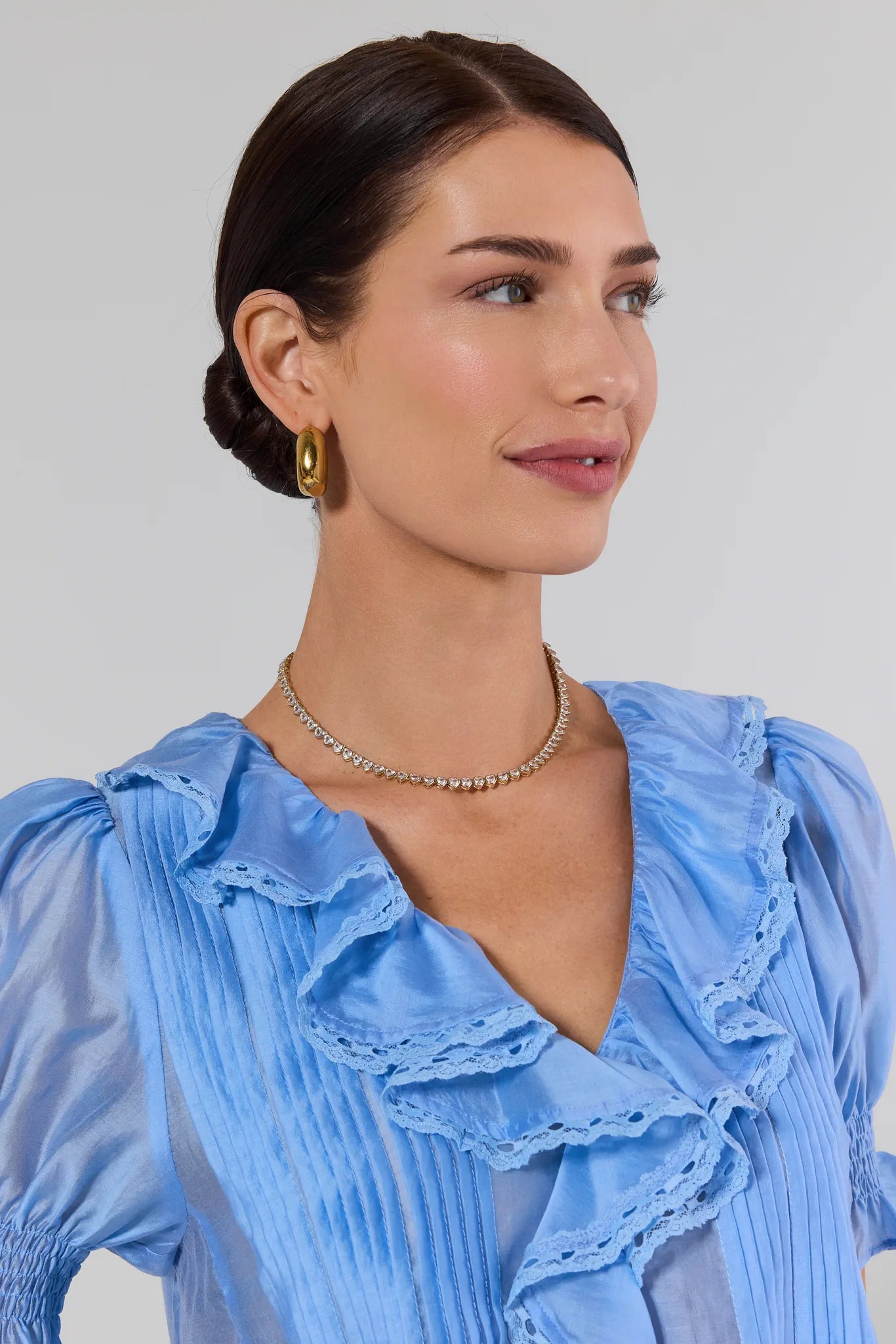 Woman wearing a light blue blouse with ruffled details on a plain background