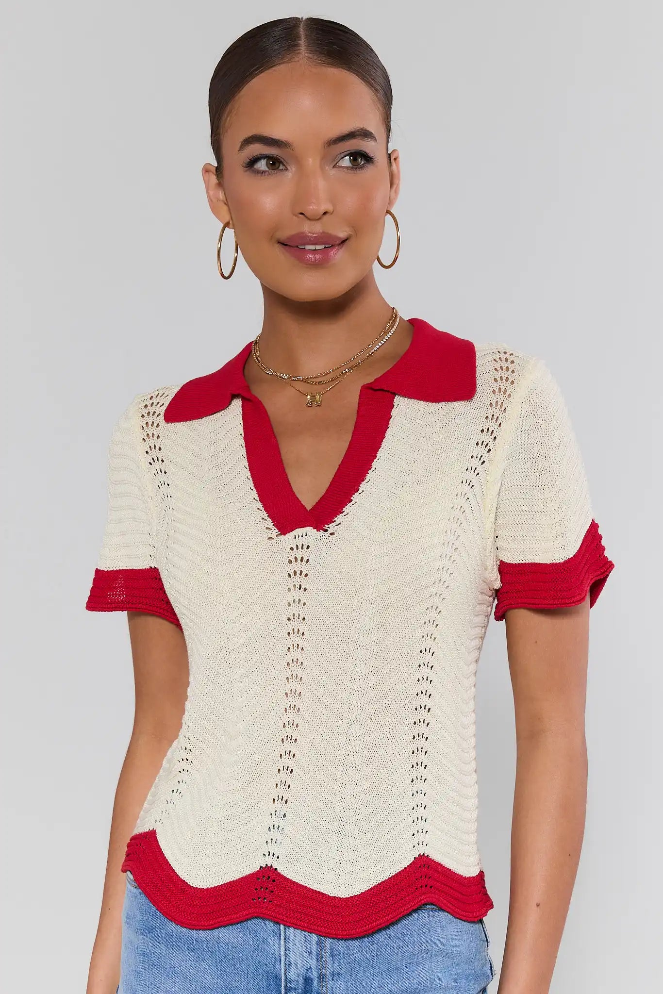 Woman wearing a cream and red top with blue jeans on a plain background