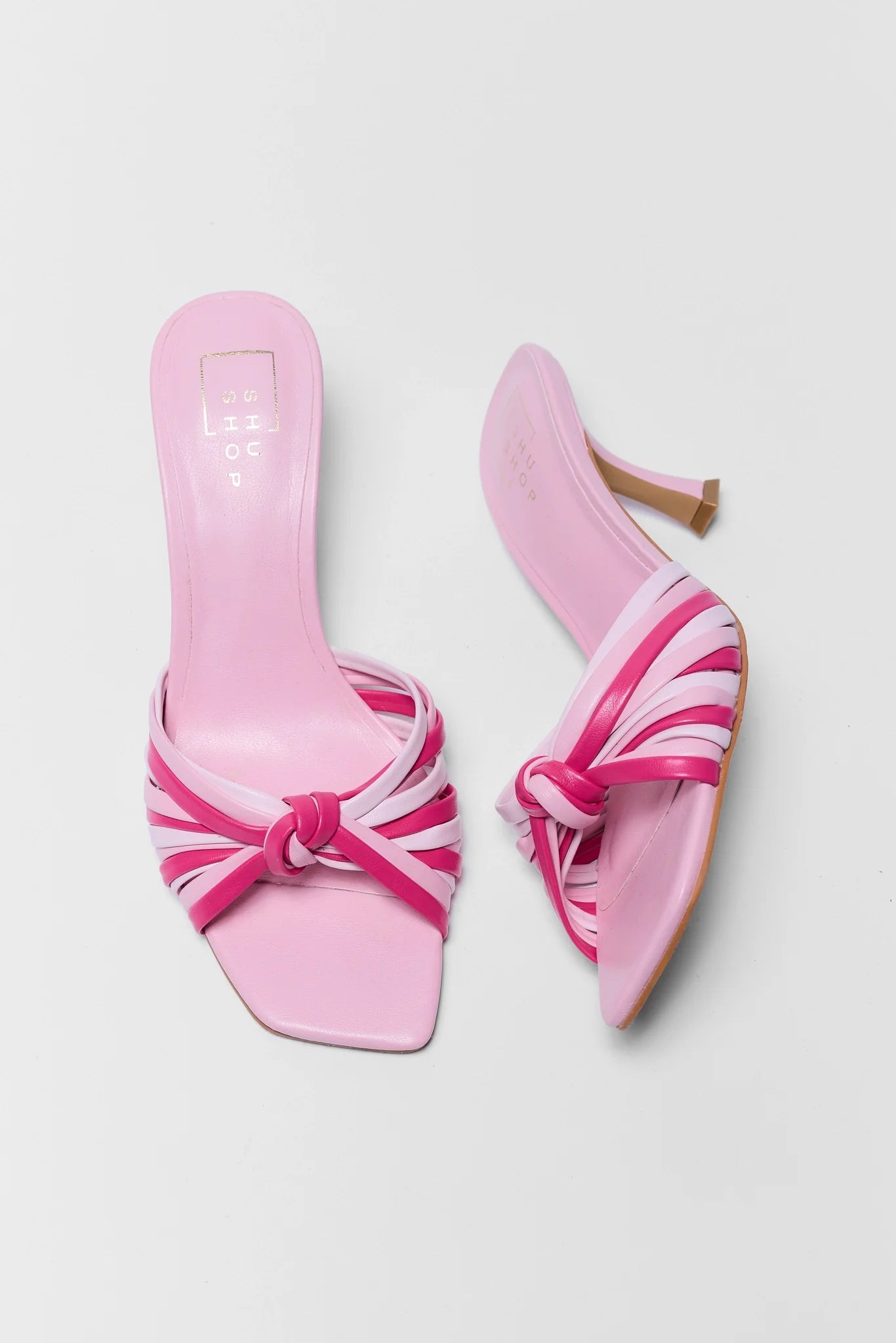 Pair of pink high-heeled shoes with a bow design on a light gray background
