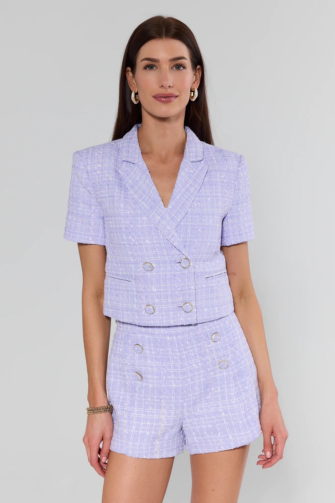 Woman wearing a light purple checkered suit with a blazer and shorts on a plain background