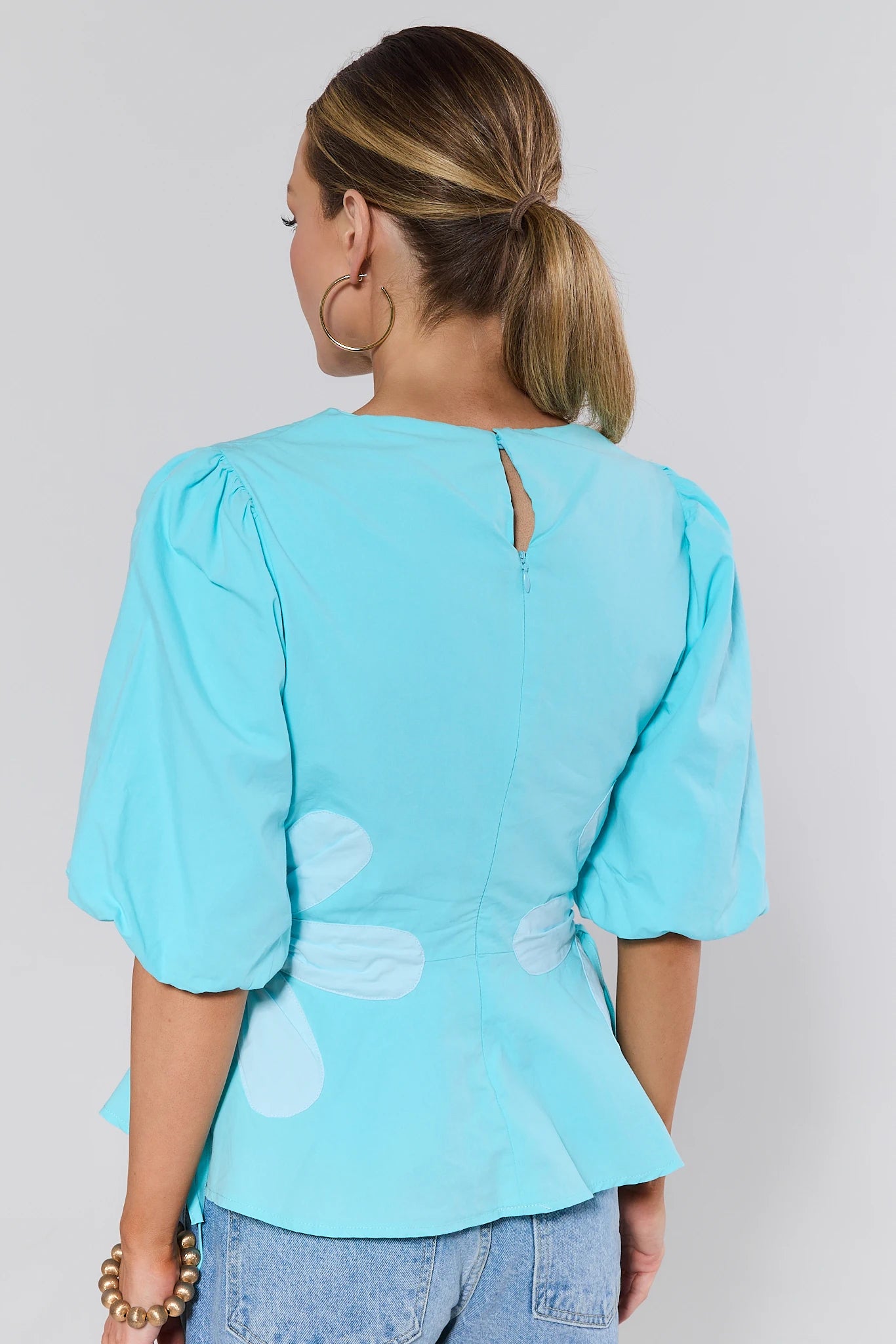 Woman wearing a light blue blouse with puff sleeves on a plain background