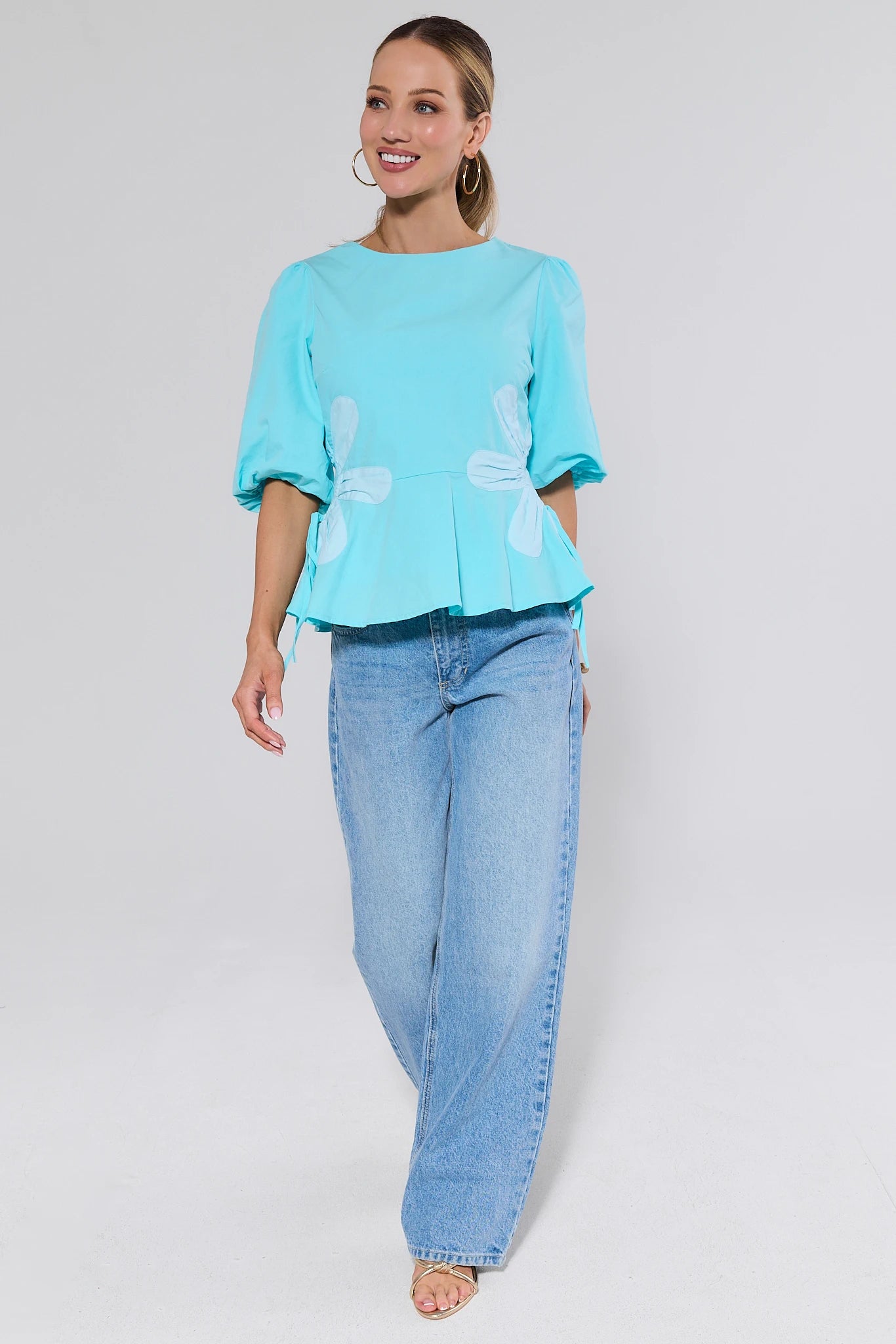 Woman wearing a light blue top and jeans on a plain background
