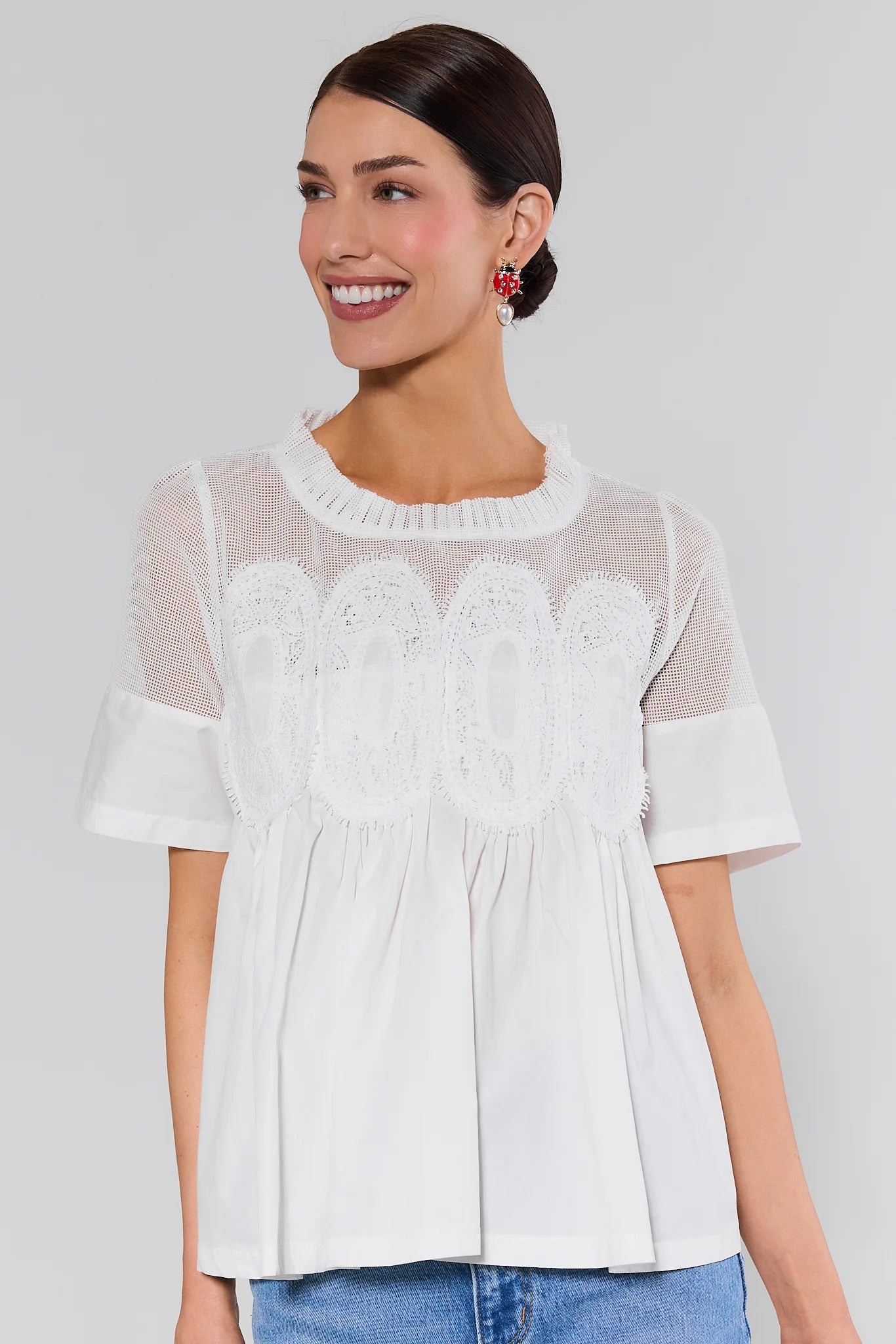 Woman wearing a white blouse with lace details and earrings on a plain background