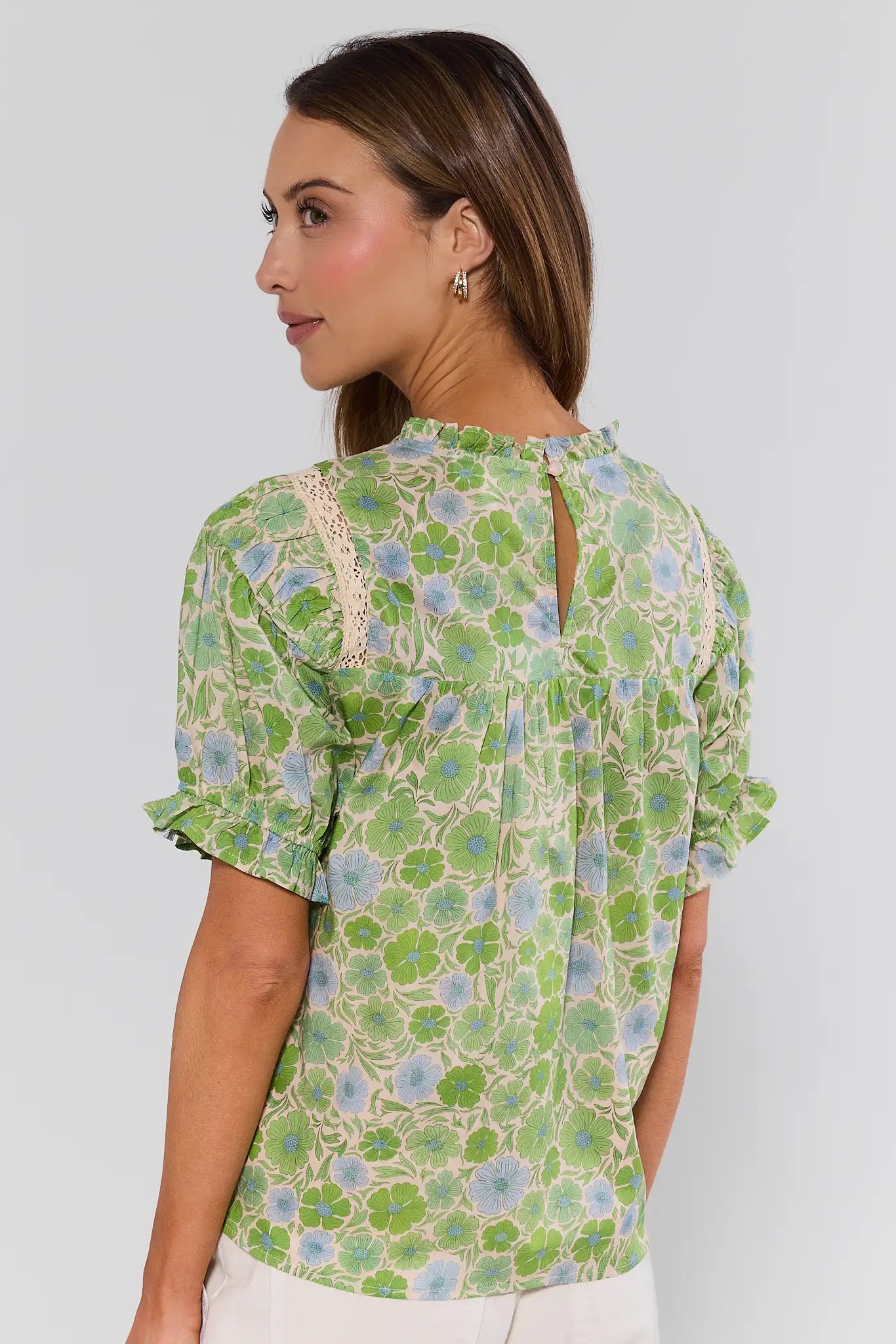 Woman standing wearing a green floral blouse against a white background