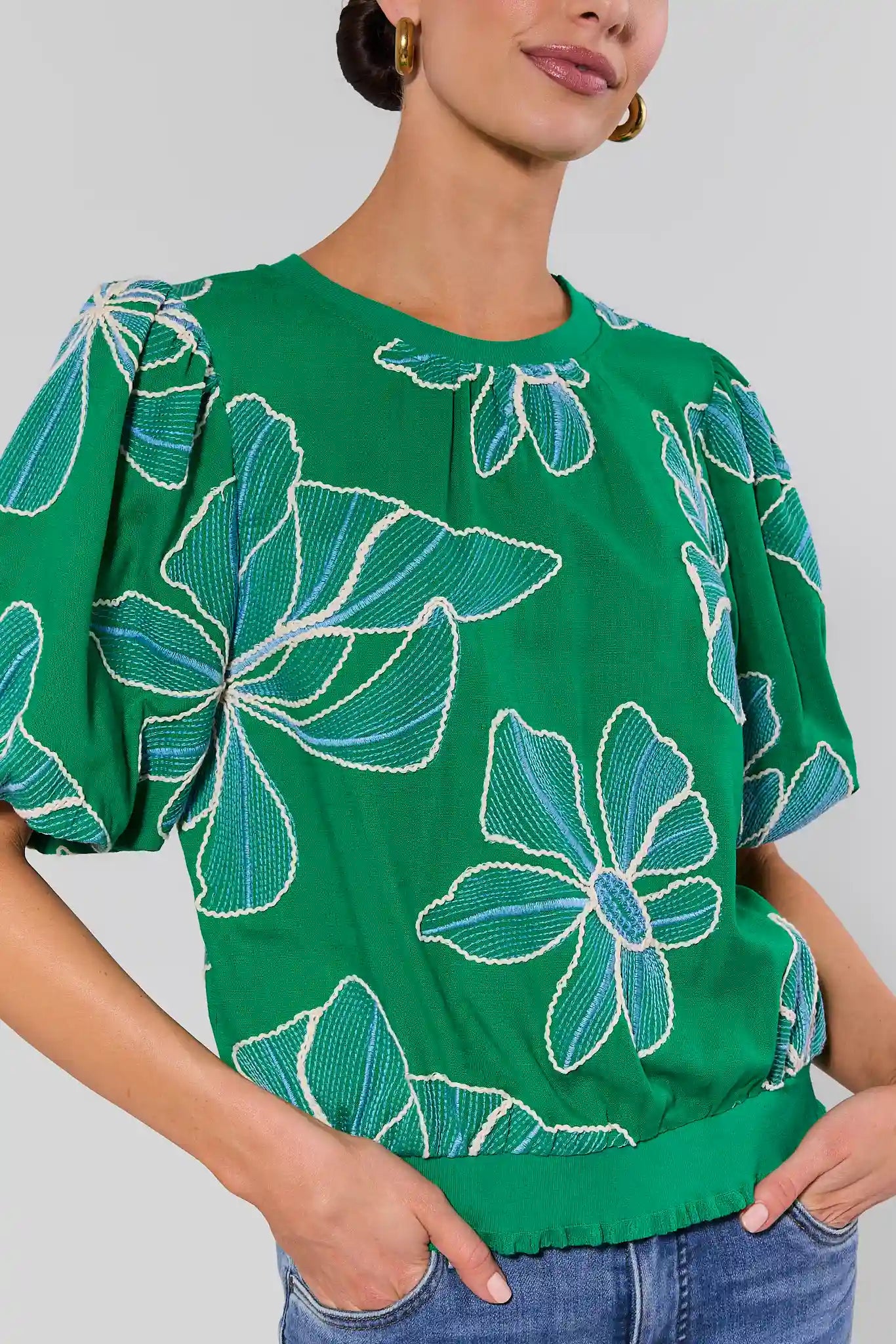 close up Green blouse with floral patterns worn by a person on a plain background