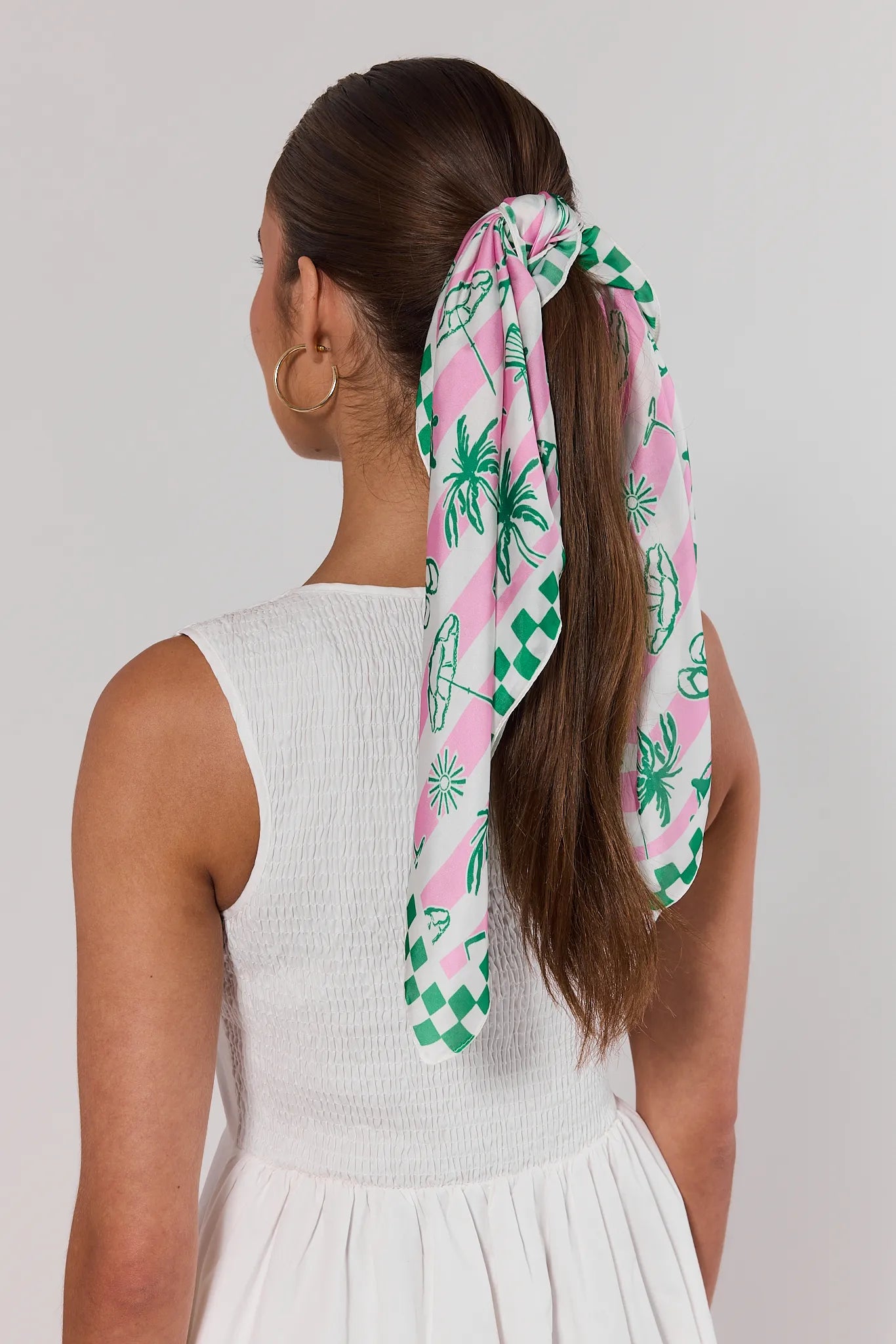 Woman with a ponytail wearing a pink and green patterned hair scarf on a plain background