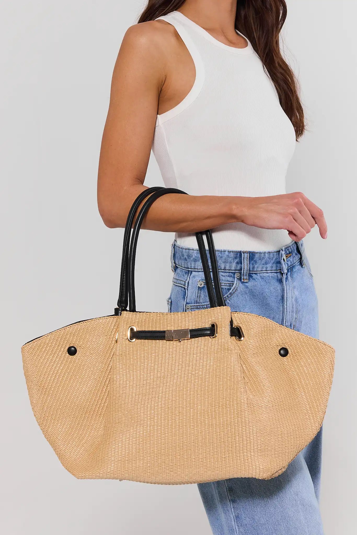 Beige straw handbag held by a person wearing a white top and blue jeans on a light gray background