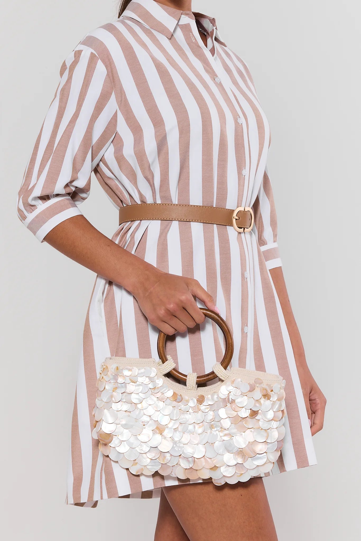 Person wearing a striped dress holding a decorative handbag against a plain background