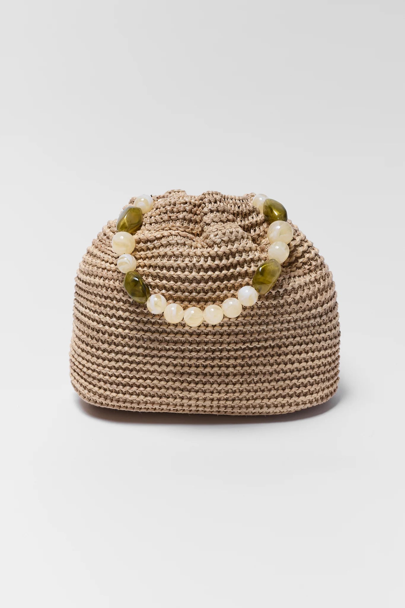 Beige woven bag with green and white beads on a light gray background