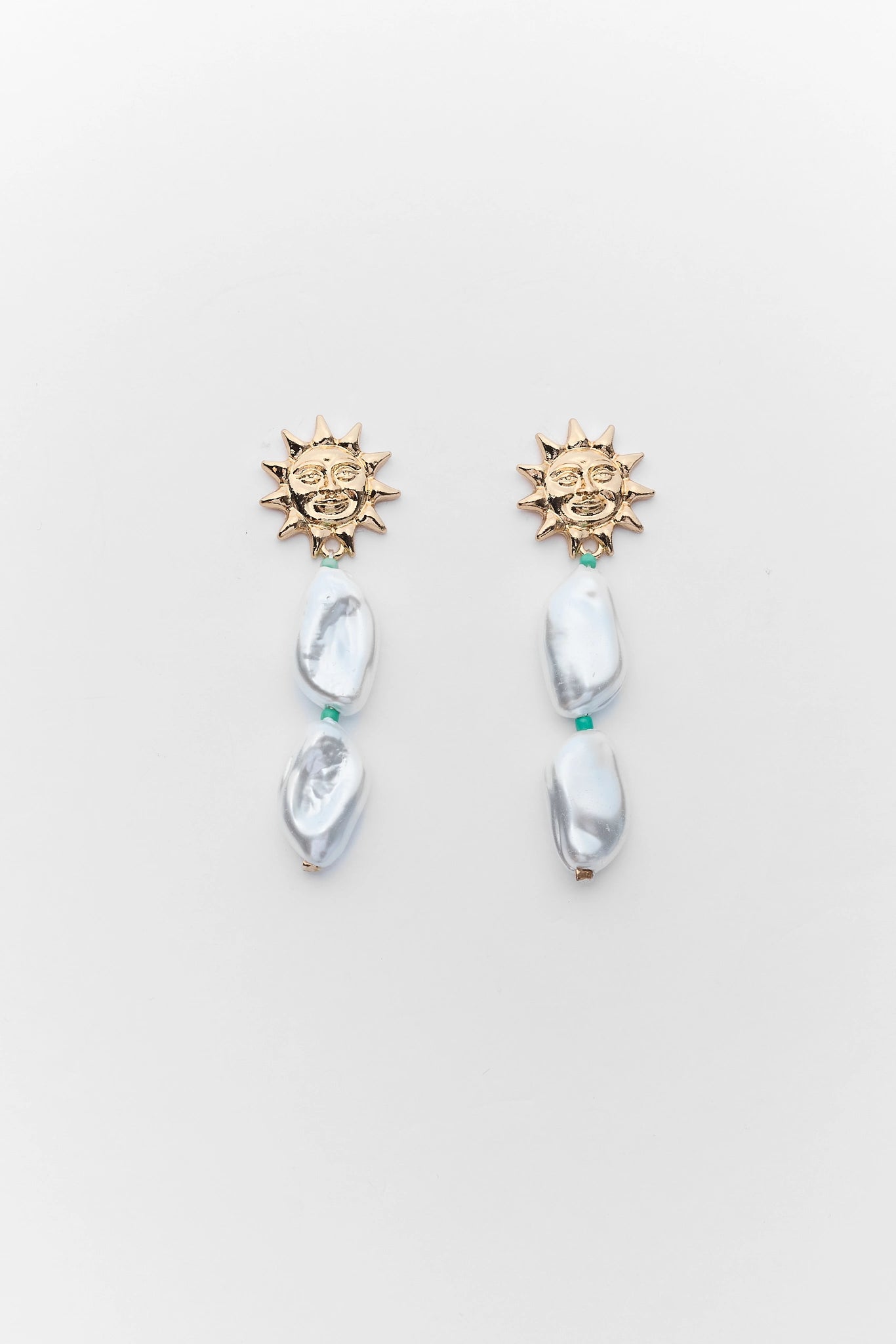 Pair of earrings with sun-like tops and pearl-like beads on a light gray background