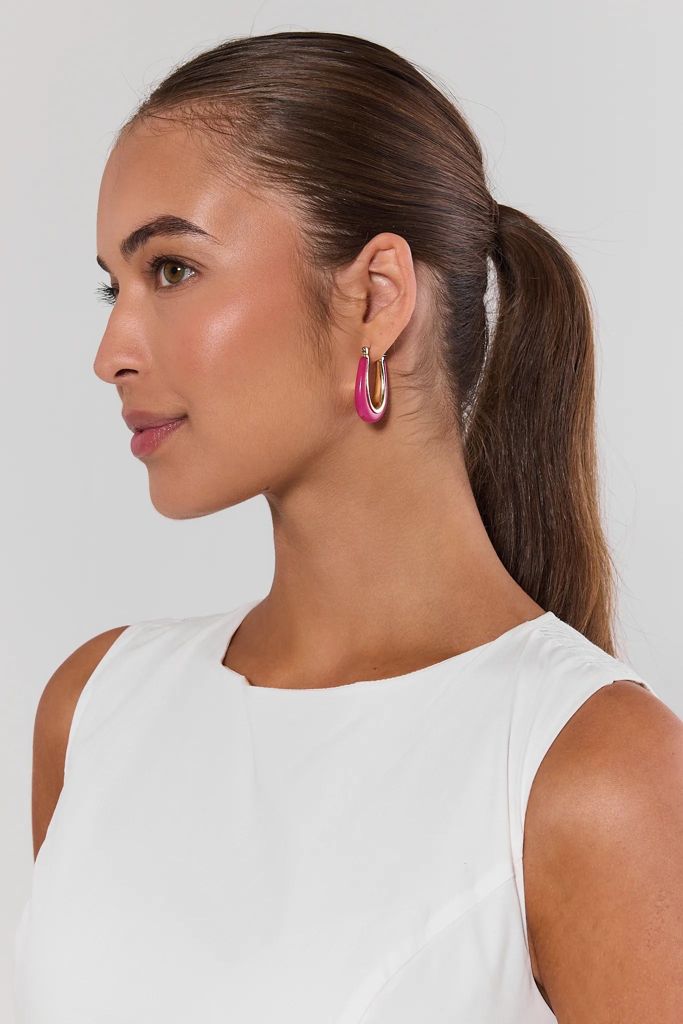 Woman with a ponytail wearing pink hoop earrings against a plain background