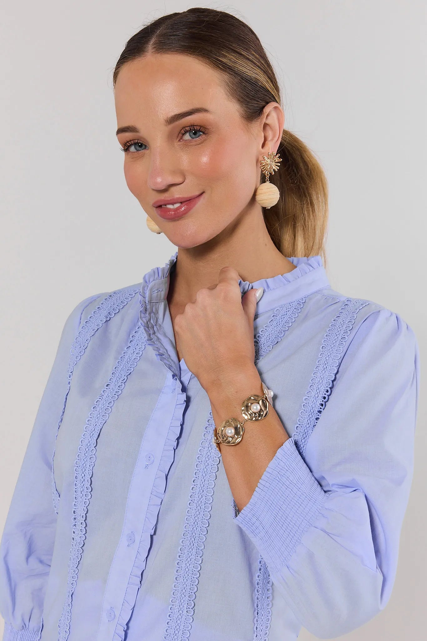 Woman wearing a light blue blouse with lace details on a plain background