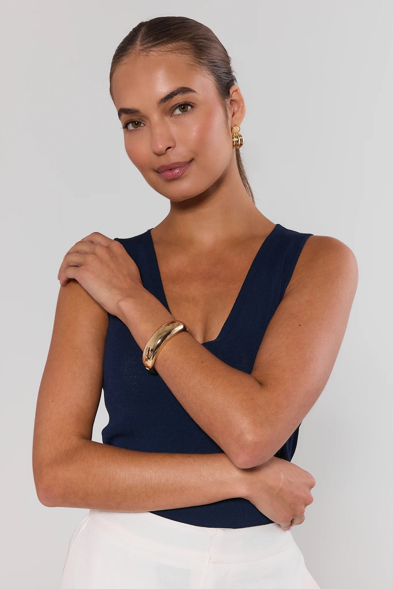 Woman wearing a navy sleeveless top with gold jewelry on a white background