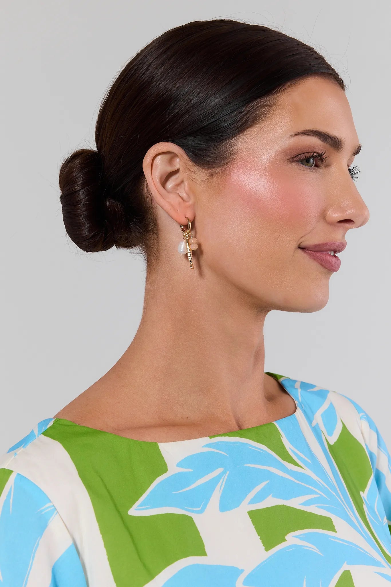 Woman wearing gold earrings and a colorful top with a floral pattern against a plain background