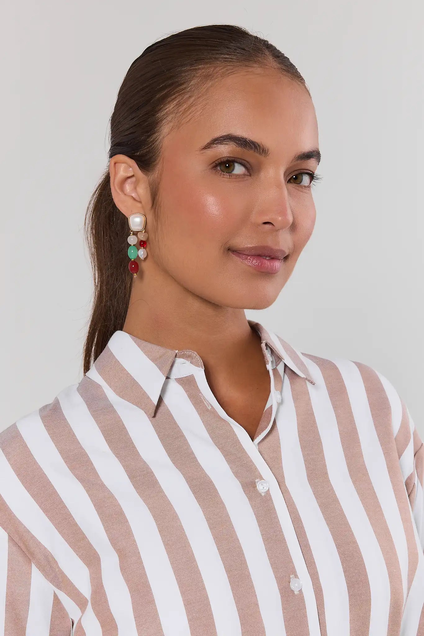 Woman wearing a striped shirt with pearl earrings against a plain background