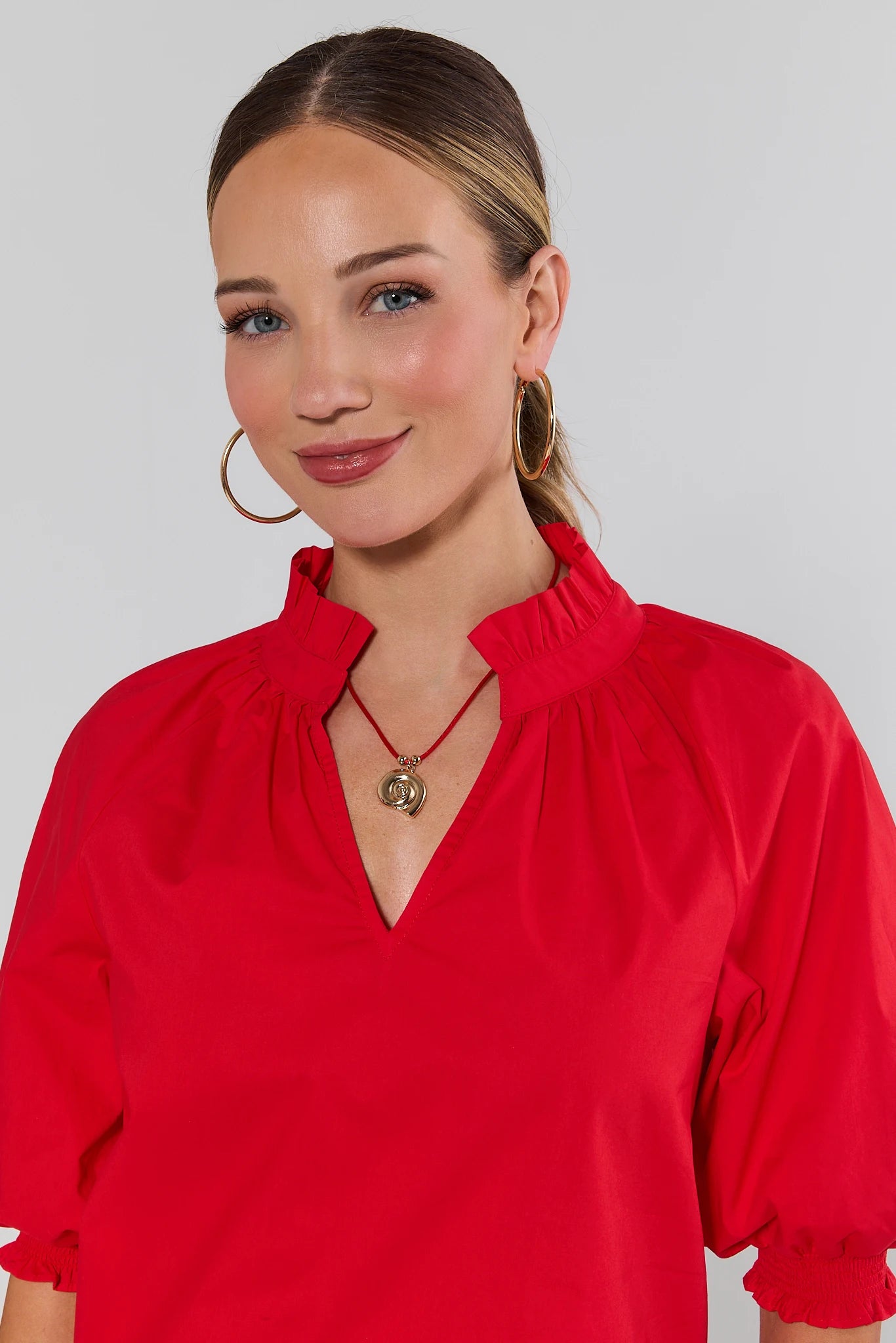 Woman wearing a red blouse with a shell necklace and plain background