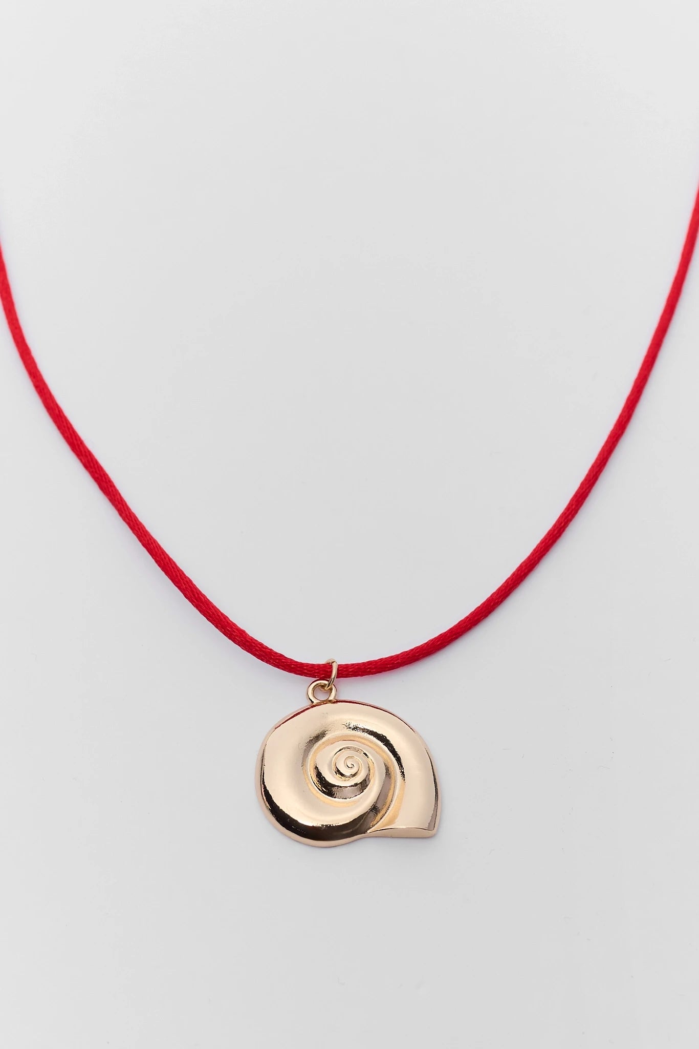 close up Necklace with a gold shell pendant on a red cord against a light gray background