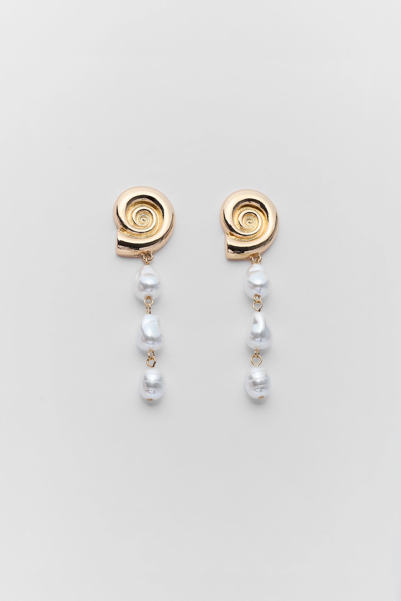 Pair of gold spiral earrings with pearl drops on a light gray background