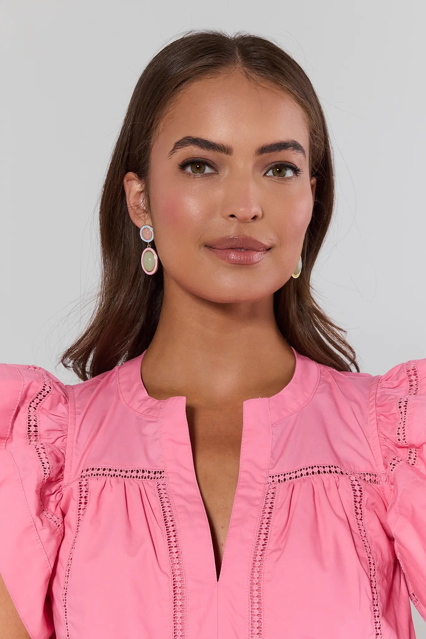 Woman wearing a pink blouse with intricate detailing on a plain background