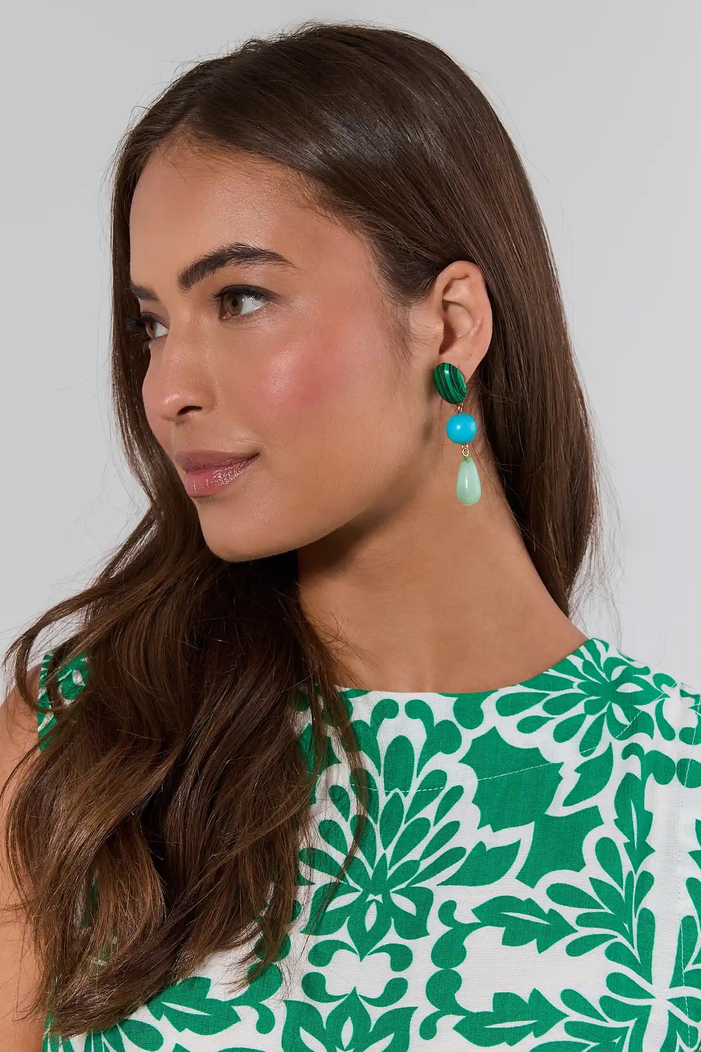 Woman wearing green earrings and a green and white patterned top against a plain background