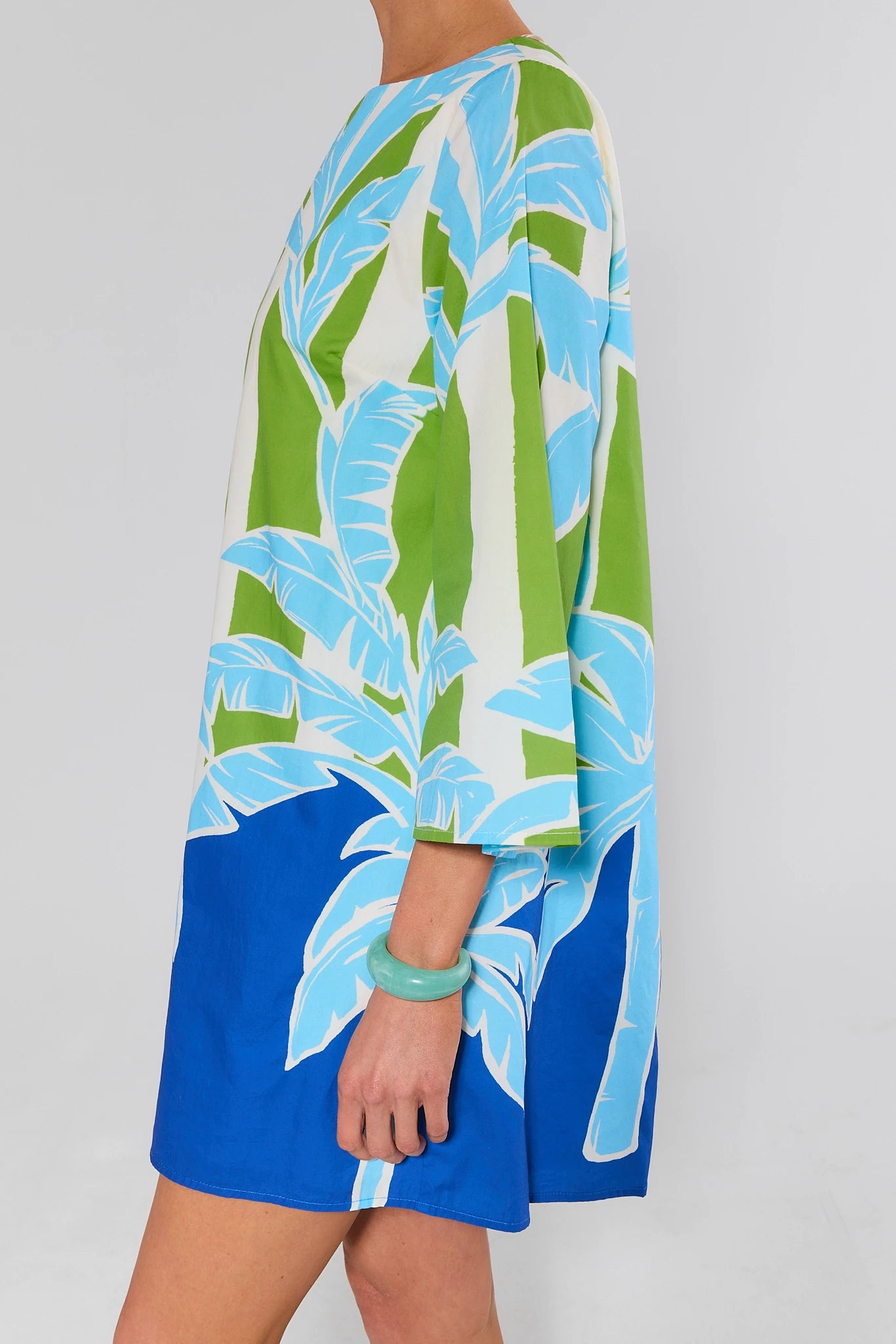 Person wearing bracelet and a colorful dress with blue, green, and white pattern on a plain background
