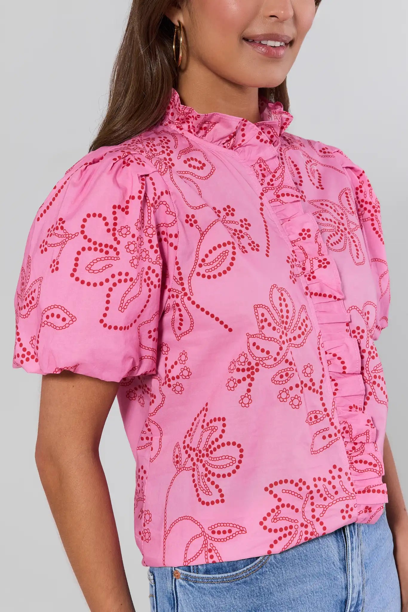 close up Person wearing a pink blouse with red floral patterns on a plain background