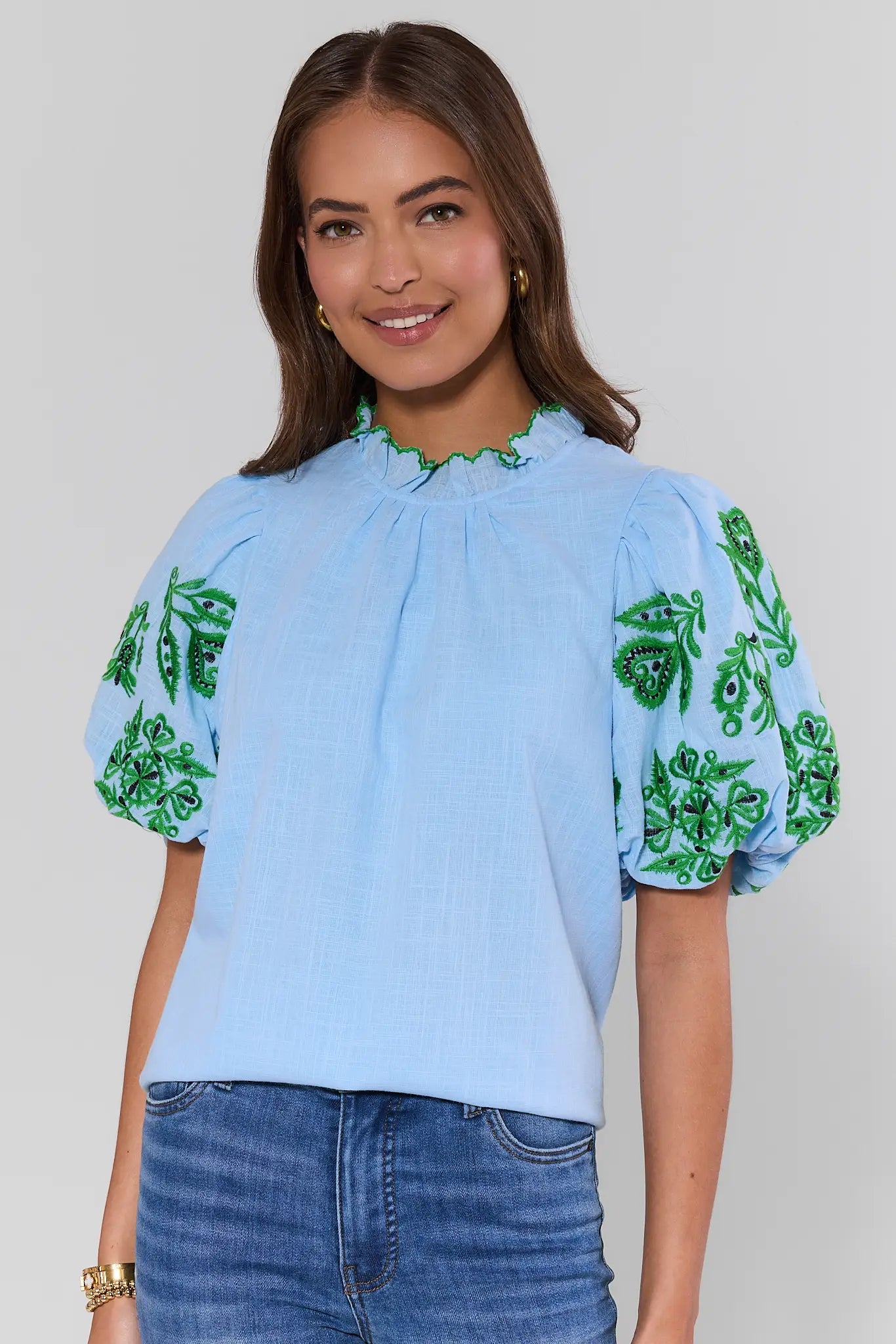 Woman wearing a light blue blouse with green floral patterns on a plain background