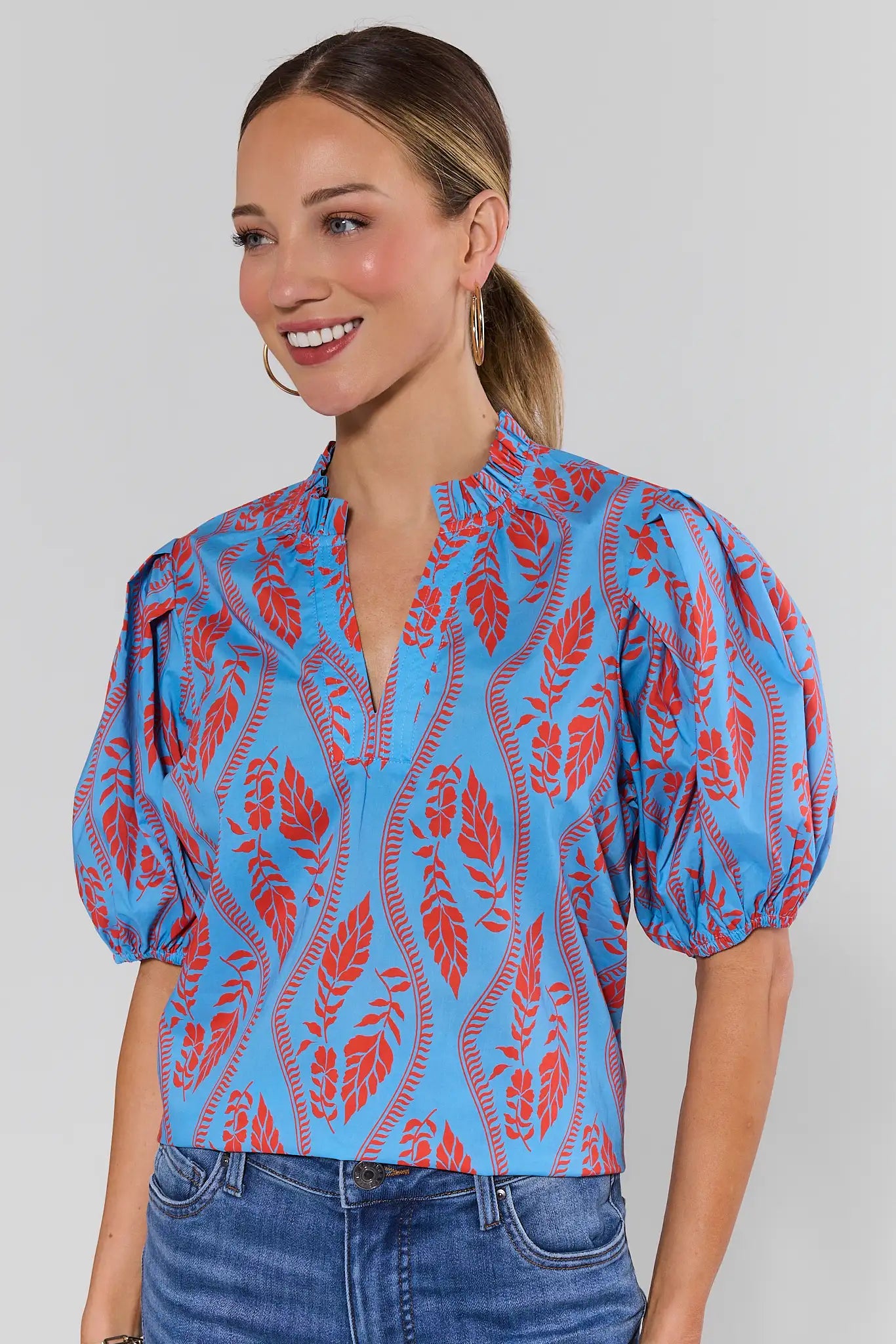 Woman wearing a blue and red patterned blouse with puffed sleeves on a plain background