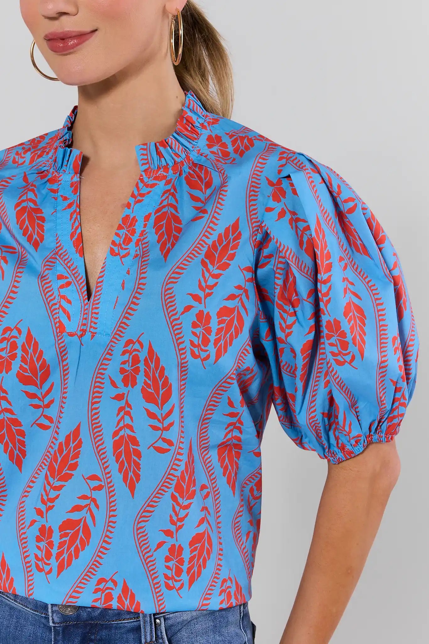 close up Woman wearing a blue blouse with red leaf pattern on a plain background